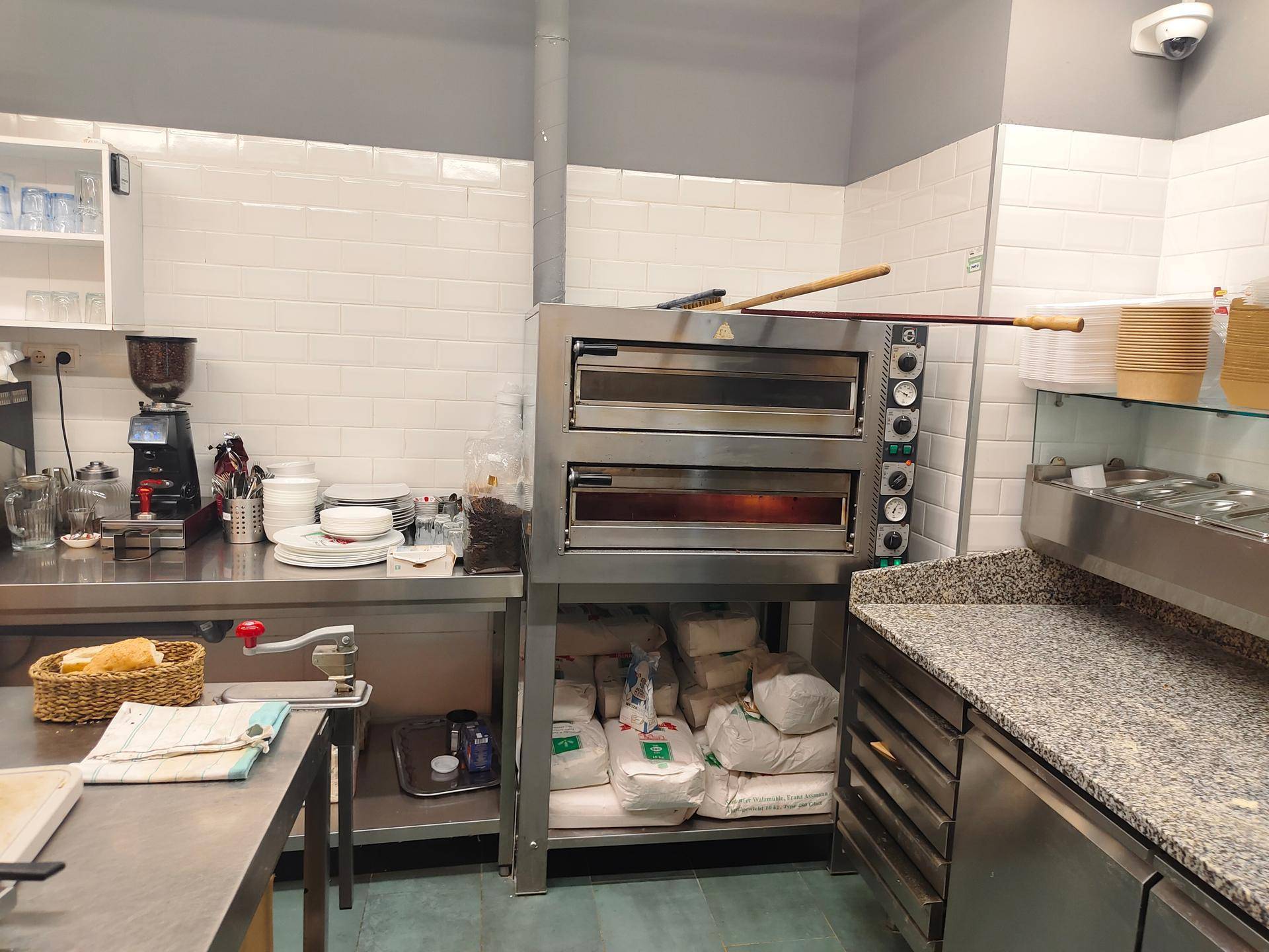 Professionelle Küche mit doppelstöckigem Pizzaofen, Edelstahl-Arbeitsflächen und weißen Fliesenwänden.