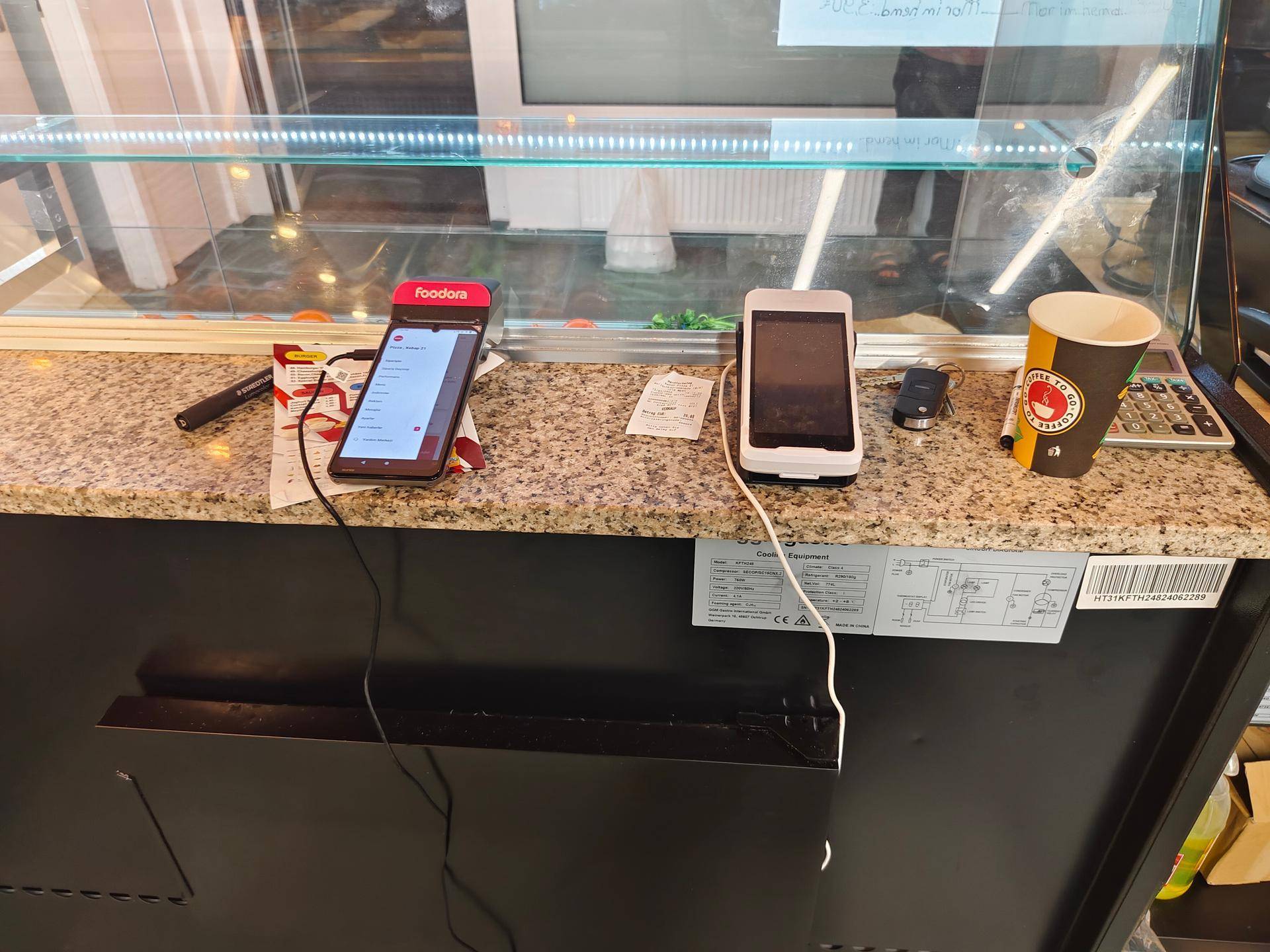 Nahaufnahme des Thekenbereichs mit zwei mobilen Bestellterminals und einem Kaffeebecher.