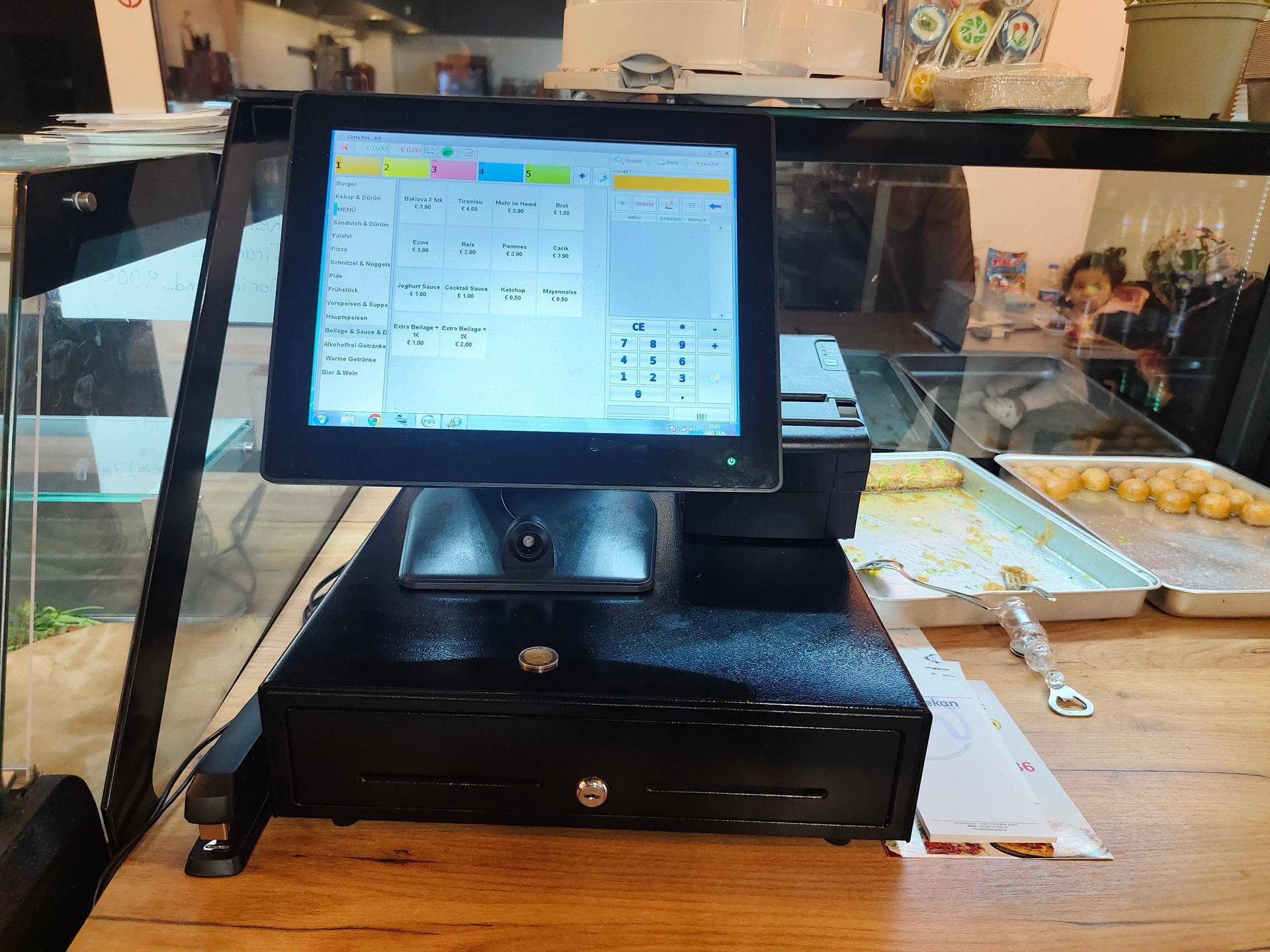 Kassensystem mit Touchscreen-Monitor und Kassenlade auf einer Holztheke.