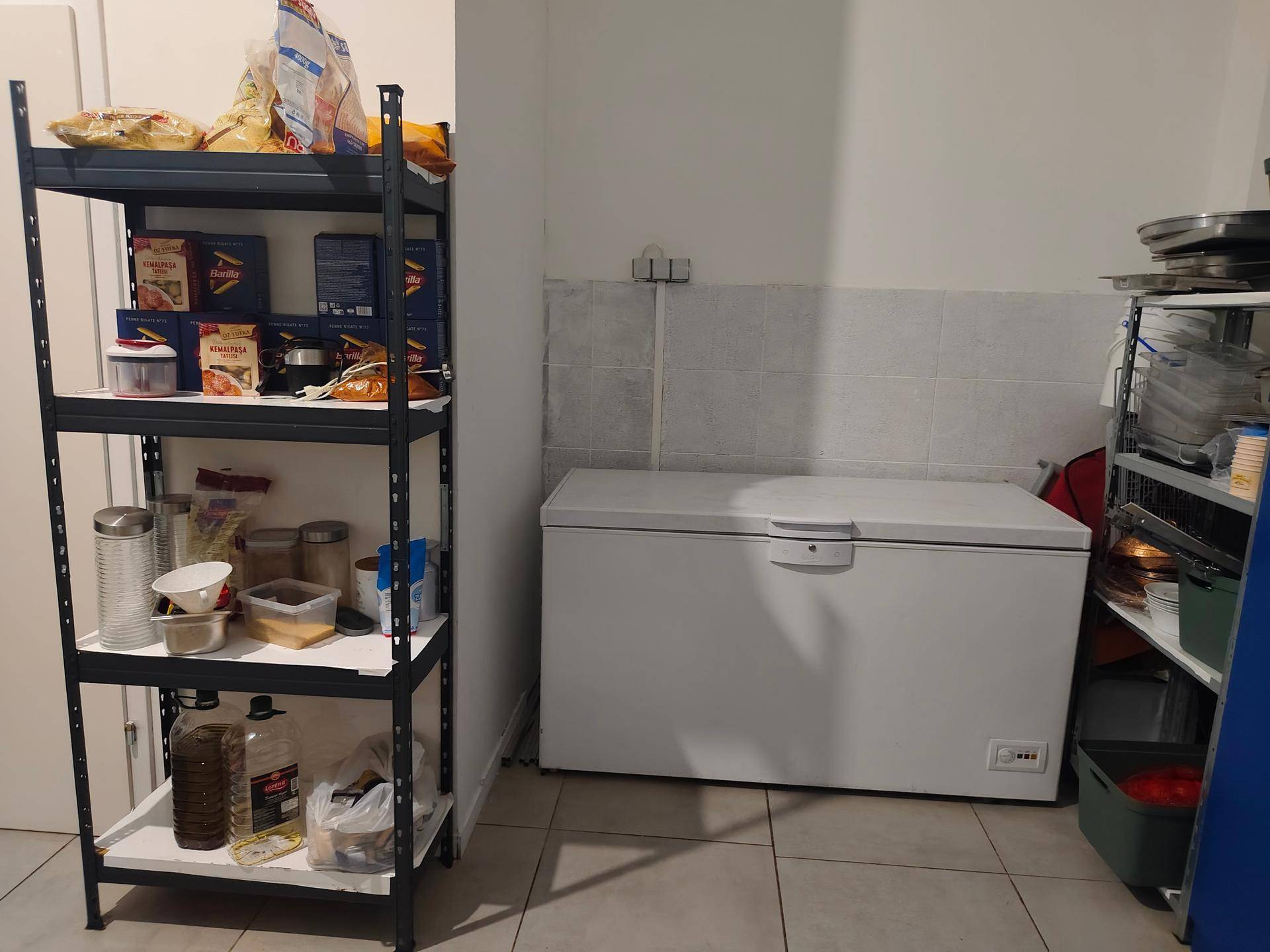 Lagerraum mit einem großen Gefrierschrank und Metallregalen voller Vorräte.