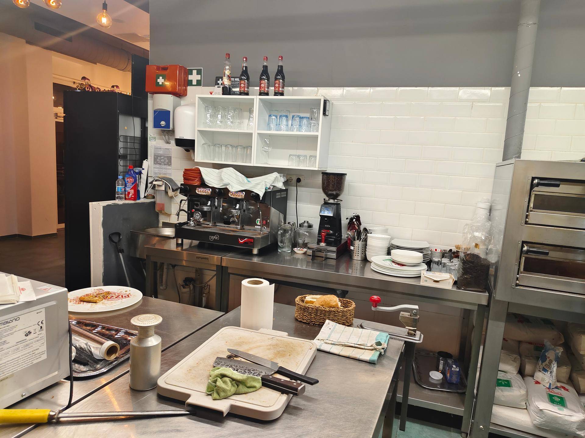 Küchenbereich mit professioneller Espressomaschine, Kaffeemühle und weiteren Küchenutensilien auf Edelstahloberflächen.