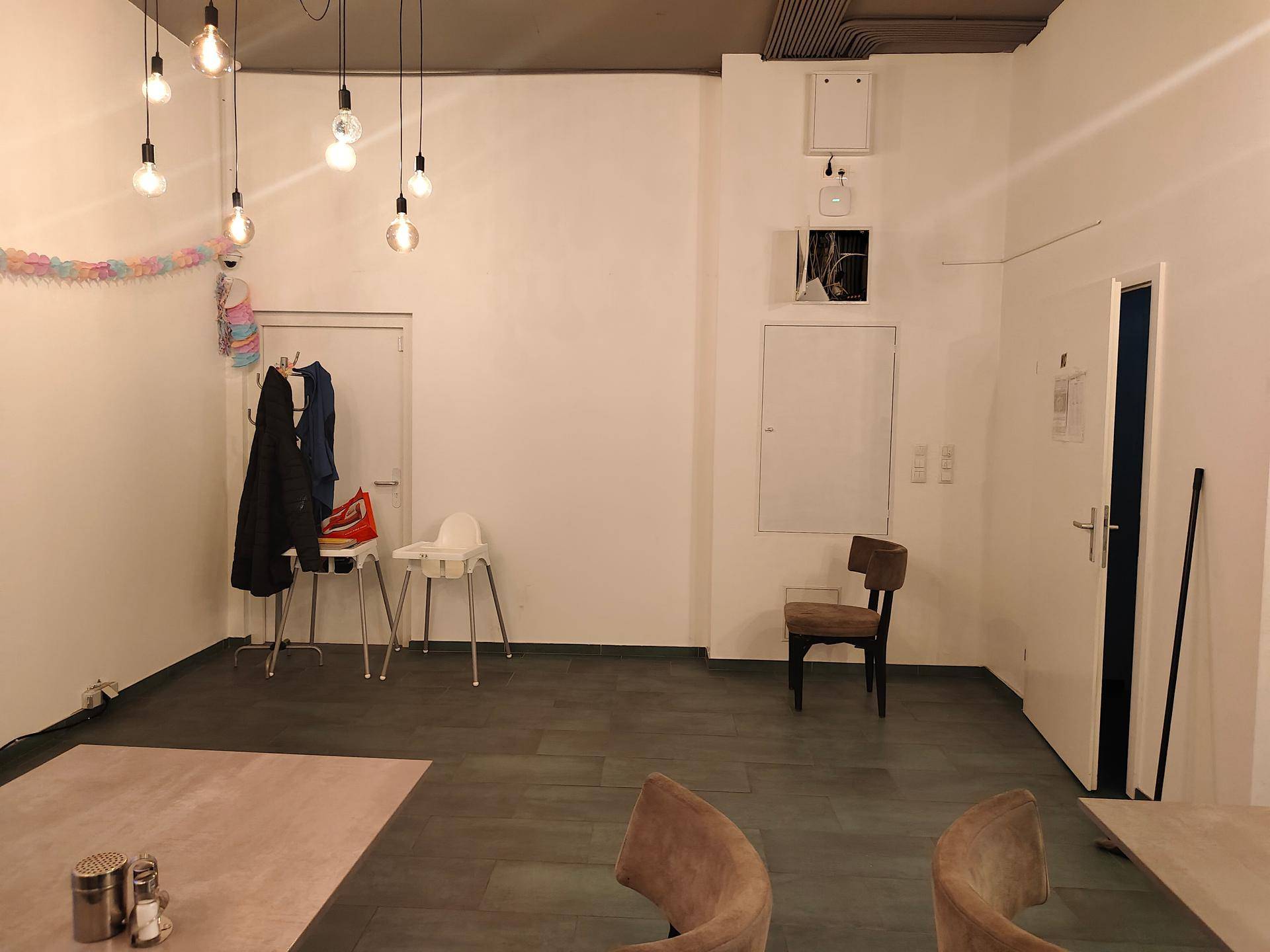 Ecke des Gastraums mit Garderobe, Babyhochstuhl und einem Stuhl, die Wände sind weiß gestrichen.