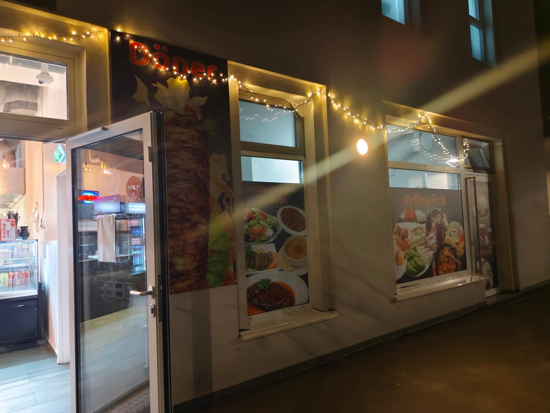 Eingangsbereich eines Geschäfts bei Nacht, geschmückt mit Lichterketten und Werbeplakaten.
