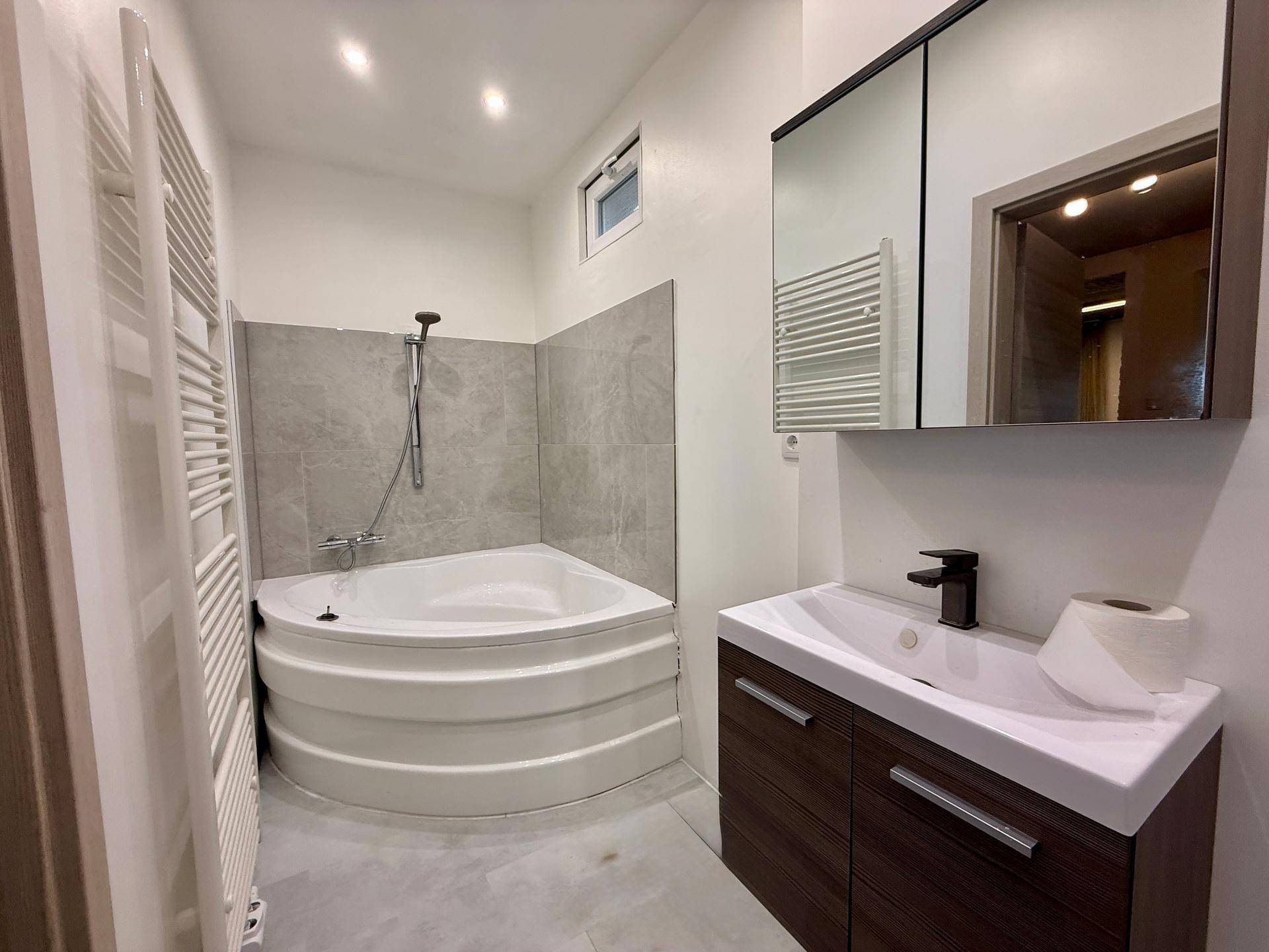 Modernes Badezimmer mit Eckbadewanne, Waschbecken und beheiztem Handtuchhalter.