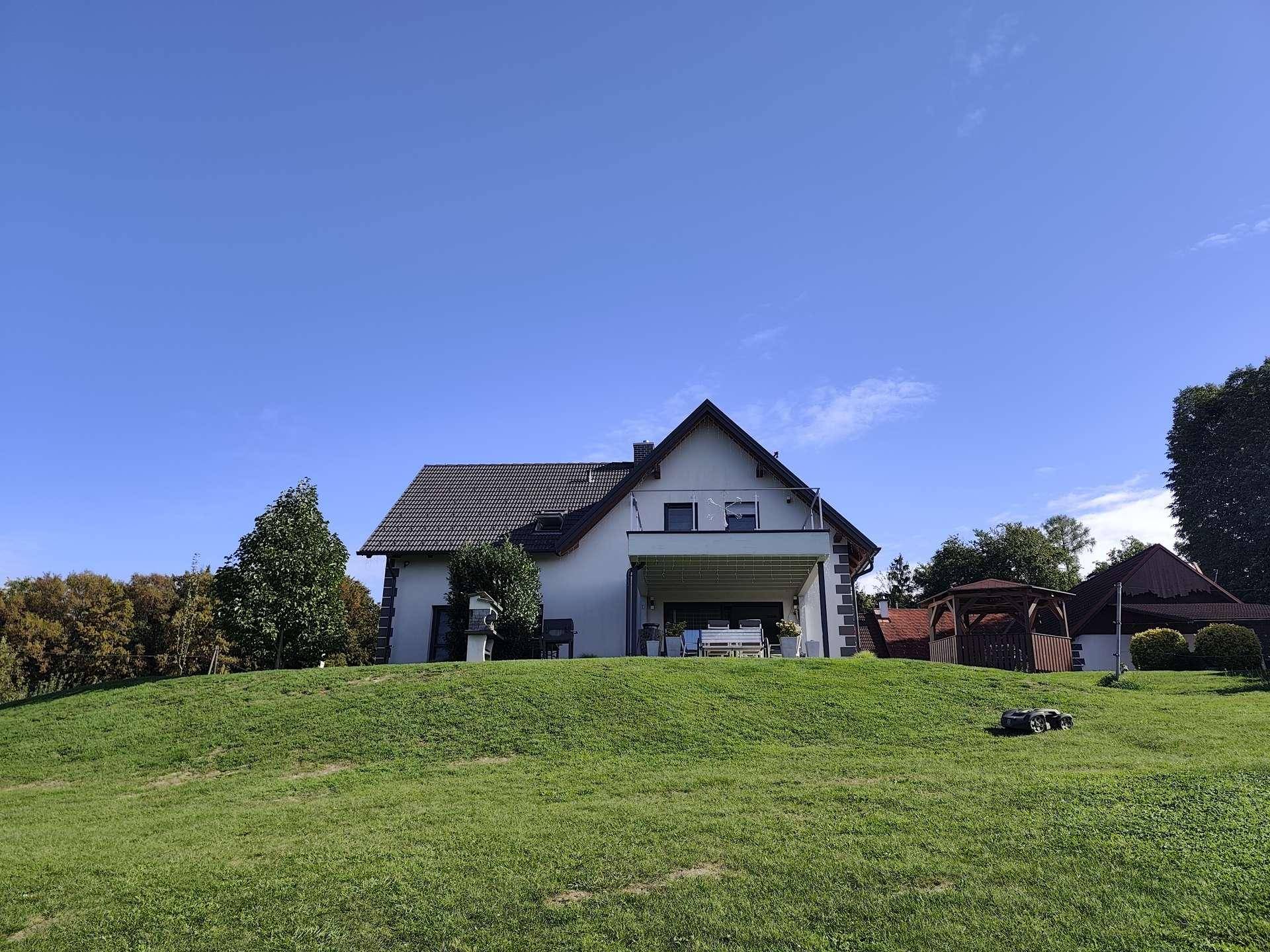 Freistehendes Einfamilienhaus mit großem Rasen und Satteldach unter blauem Himmel.