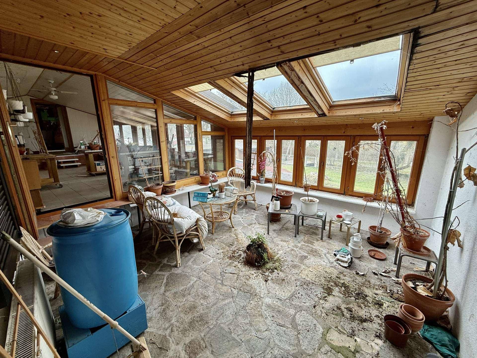 Großer Wintergarten mit Steinboden, vielen Pflanzen und Oberlichtern, ideal zum Entspannen.