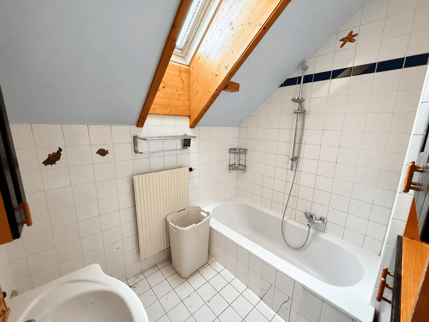 Helles Badezimmer mit Badewanne, Dachfenster und weißen Fliesen.