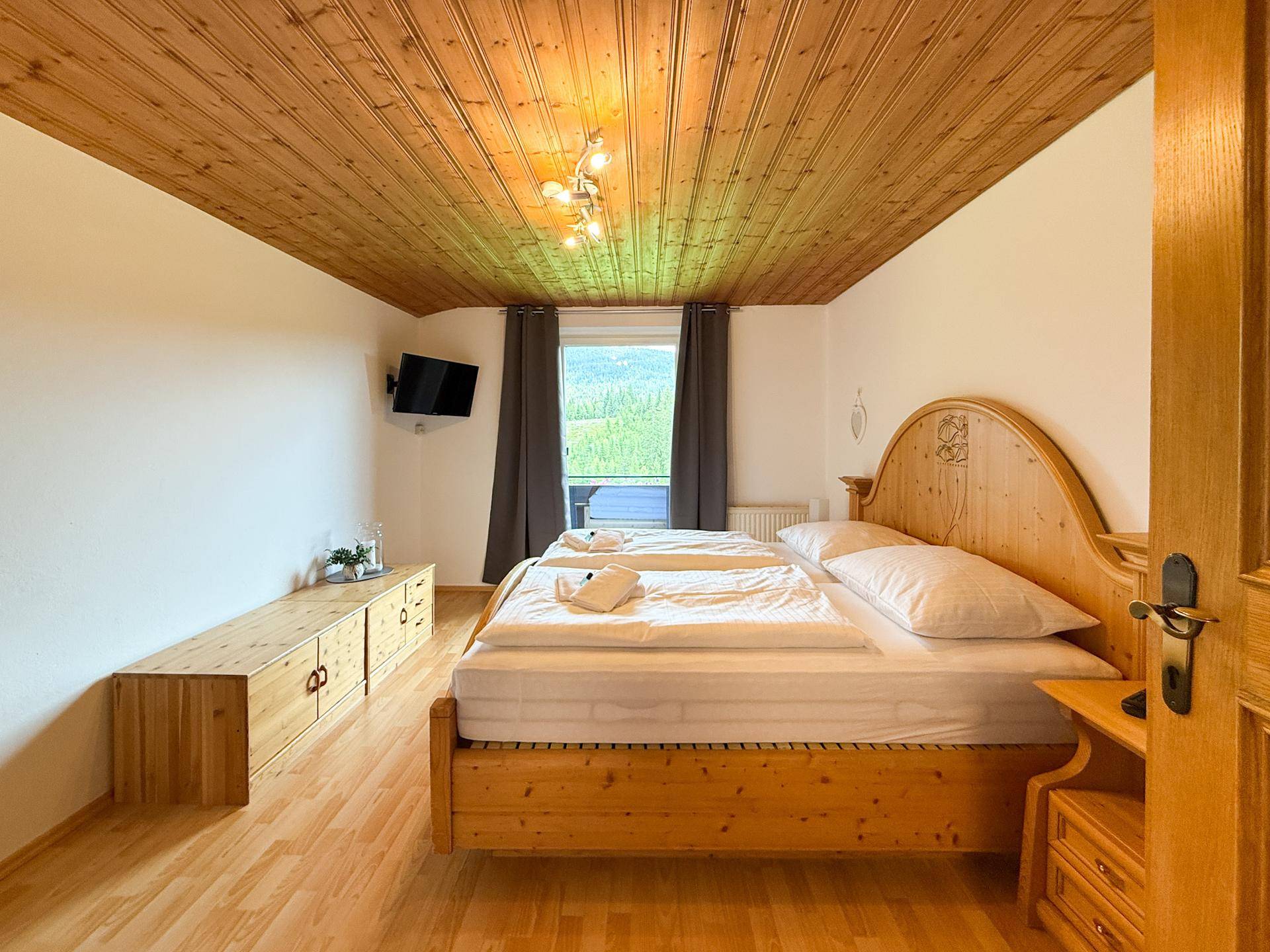 Helles Schlafzimmer mit Holzdoppelbett, Holzboden und Fenster mit Blick auf die Landschaft.
