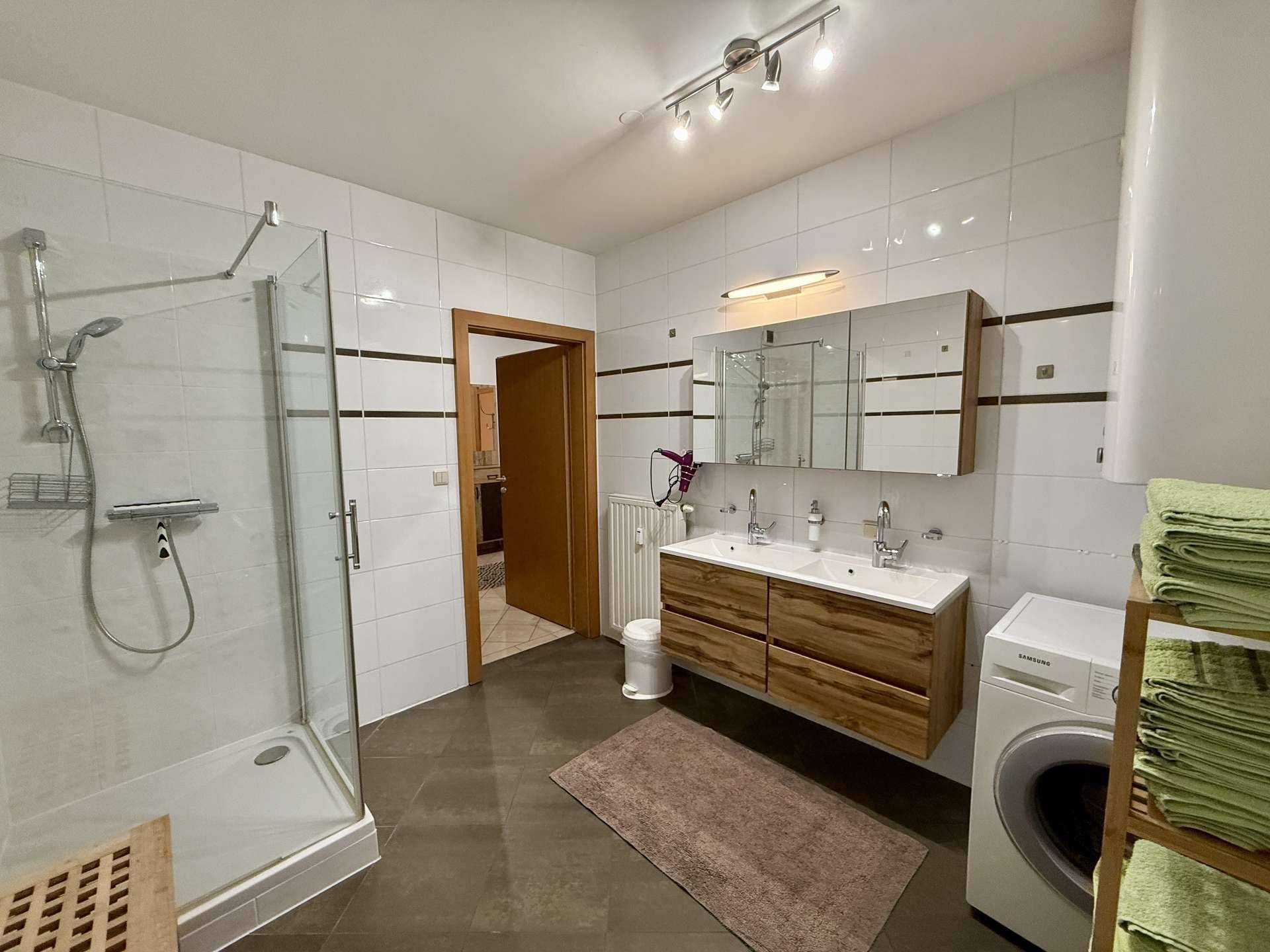 Modernes Badezimmer mit Doppelwaschbecken, großer Duschkabine und Waschmaschine.