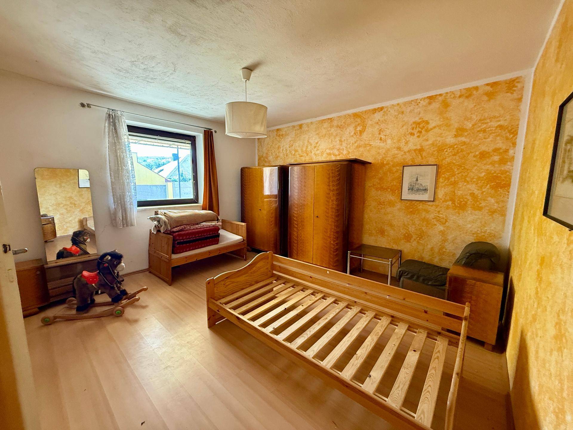 Schlafzimmer mit Holzboden, rustikalen Möbeln und lebhafter Wandgestaltung in Gelbtönen.