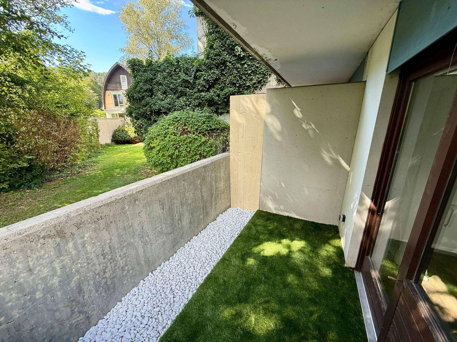 Sonniger Balkon mit Kunstrasen und Blick auf den Garten und umliegende Häuser.