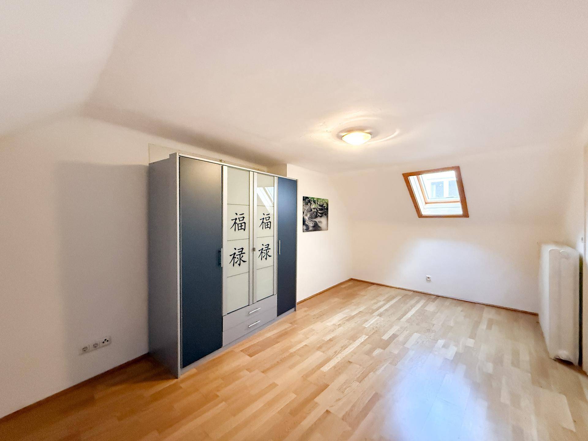 Schlafzimmer im Dachgeschoss mit Holzboden, Kleiderschrank und Dachfenster.