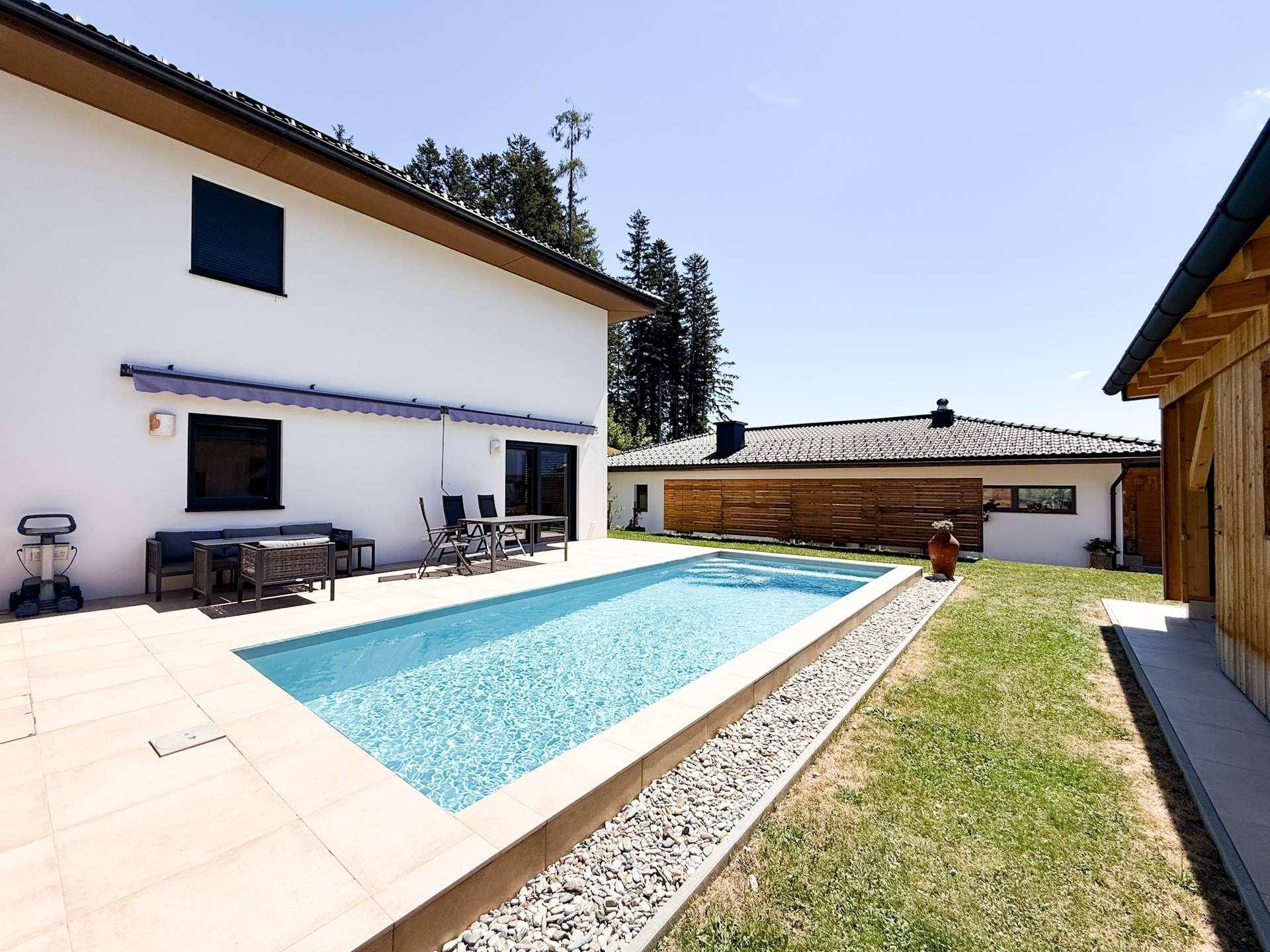 Weitläufiger Außenbereich mit Pool, Sonnenterrasse und moderner Hausfassade.