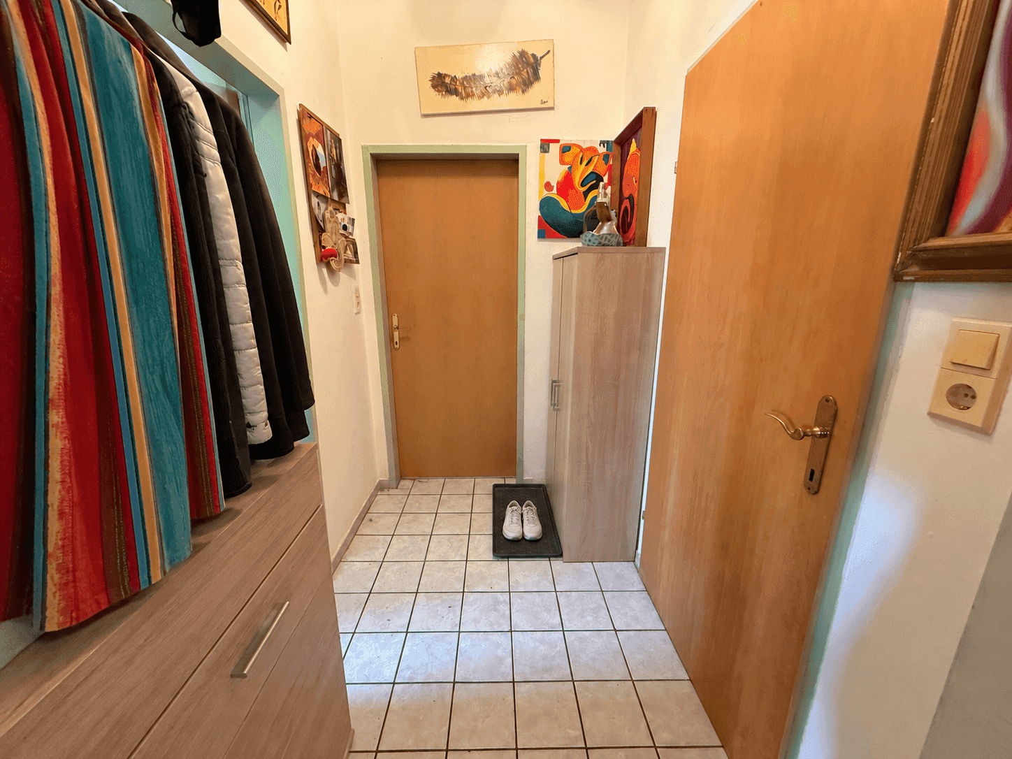 Eingangsbereich mit Fliesenboden, Garderobe und bunten Kunstwerken an den Wänden.