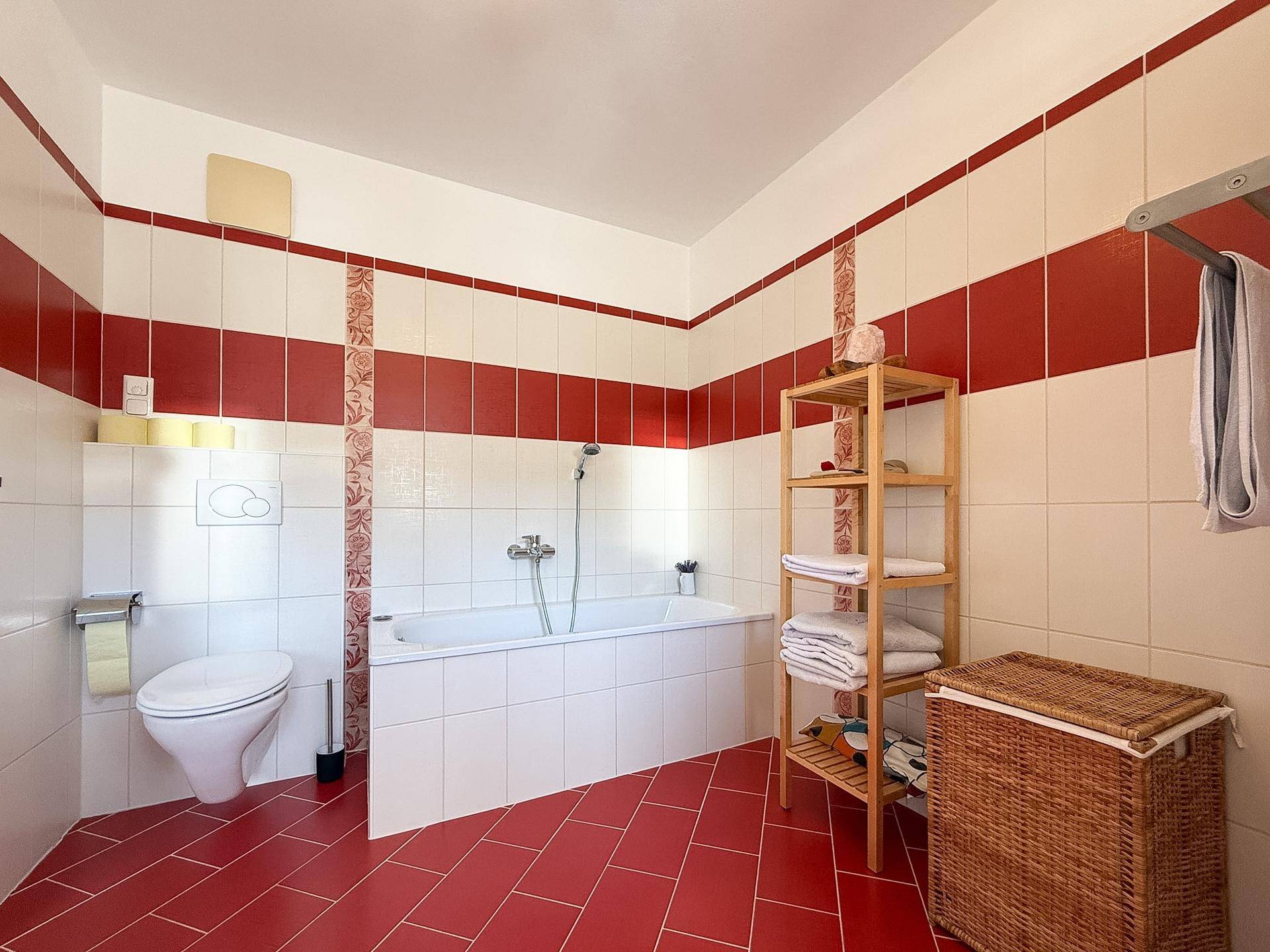 Geräumiges Badezimmer mit Badewanne, roten und weißen Fliesen und WC.