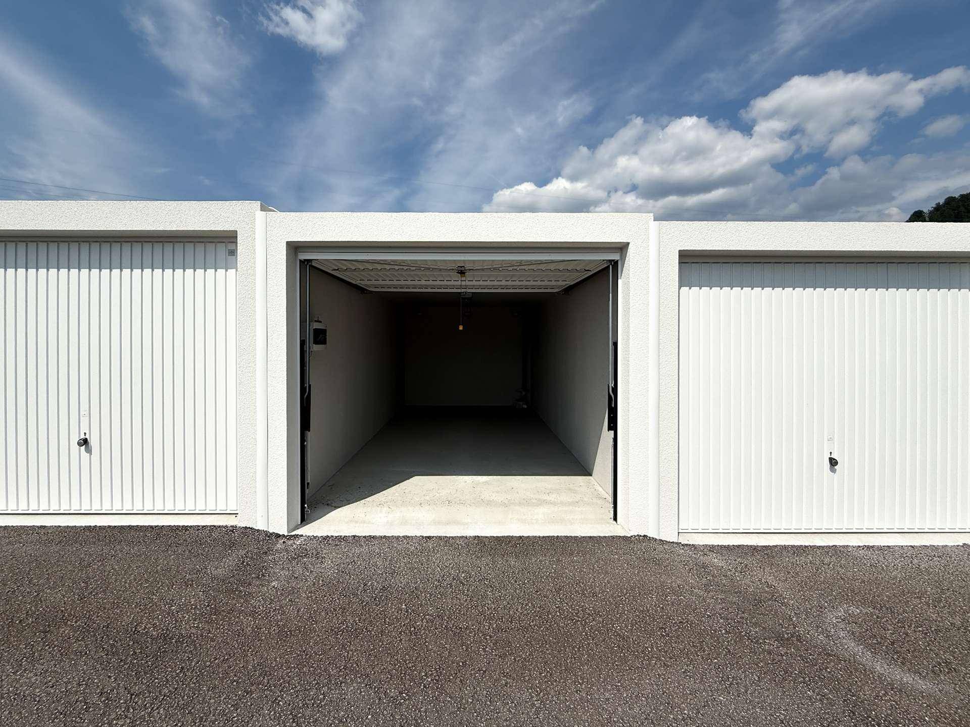 Drei moderne Garagenboxen mit weißen Toren, die mittlere ist geöffnet und zeigt den Innenraum.