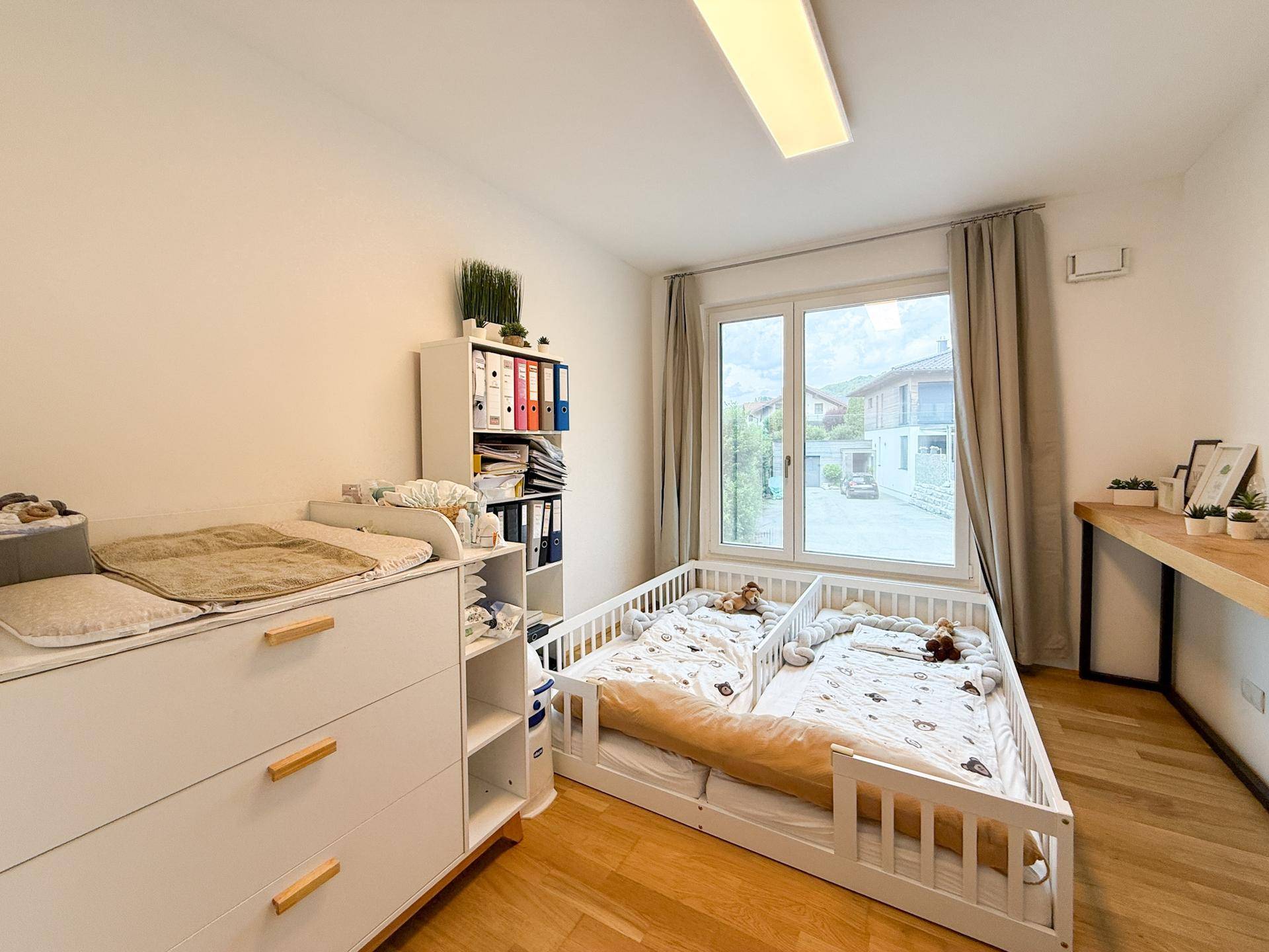 Kinderzimmer mit zwei Betten, Wickelkommode und hellem Holzboden.