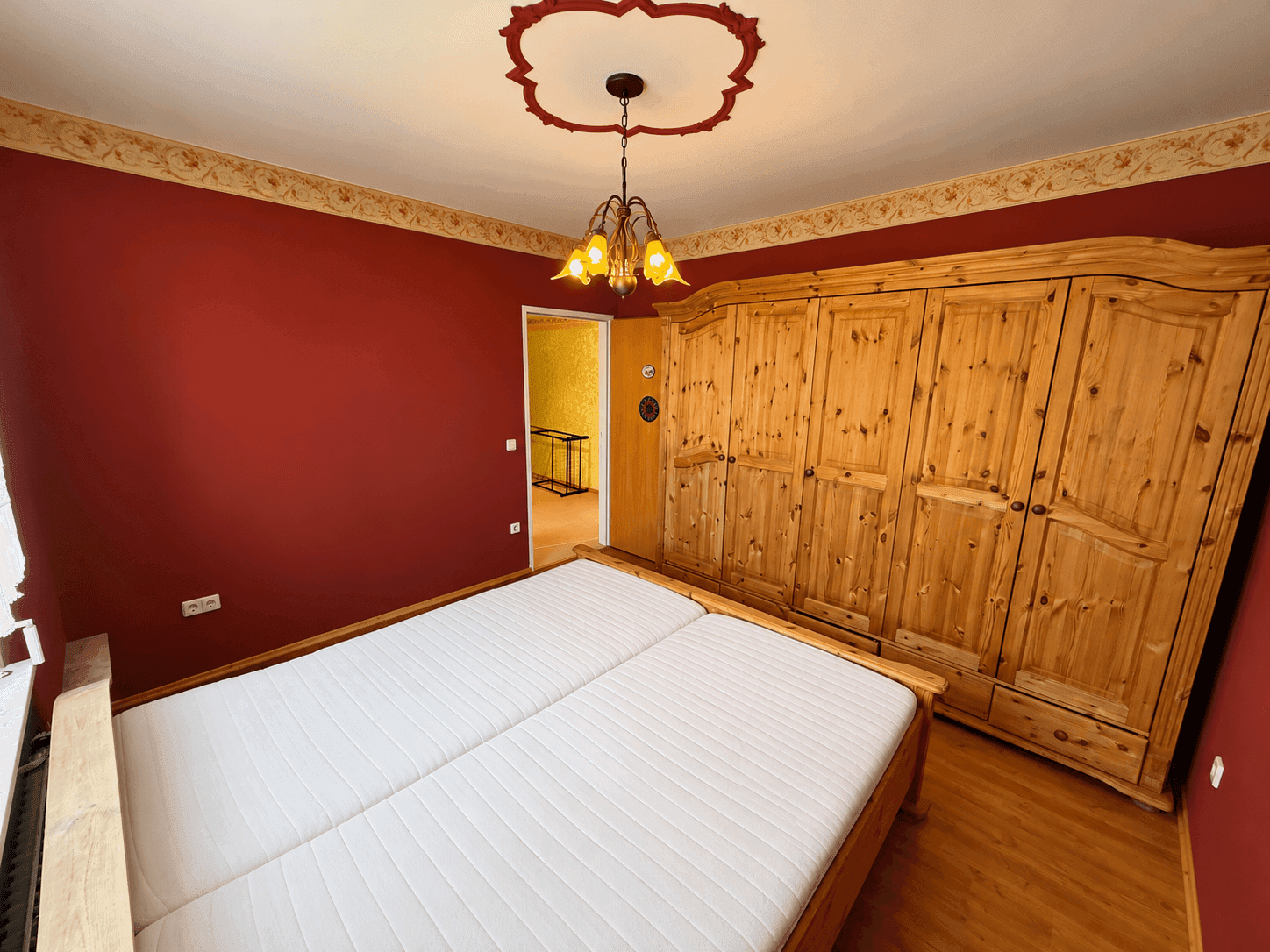 Schlafzimmer mit Doppelbett, großem Holzschrank und roter Wandgestaltung.