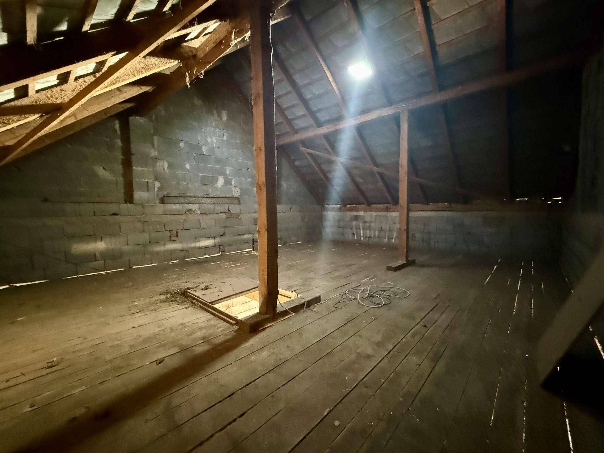 Dachboden mit sichtbarer Holzkonstruktion, Ziegelwänden und Holzdielenboden.