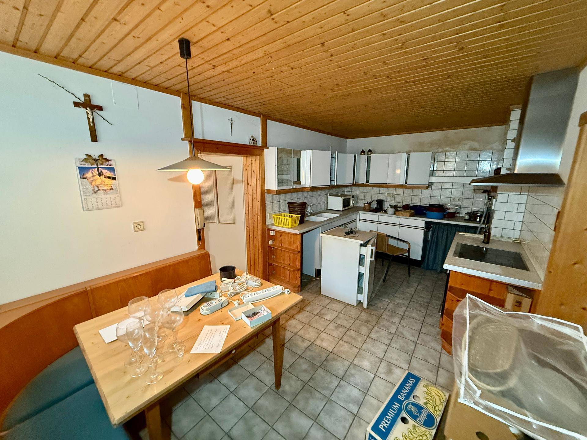 Küche mit Essbereich, weißen Schränken, Fliesenboden und Holzdecke im Landhausstil.