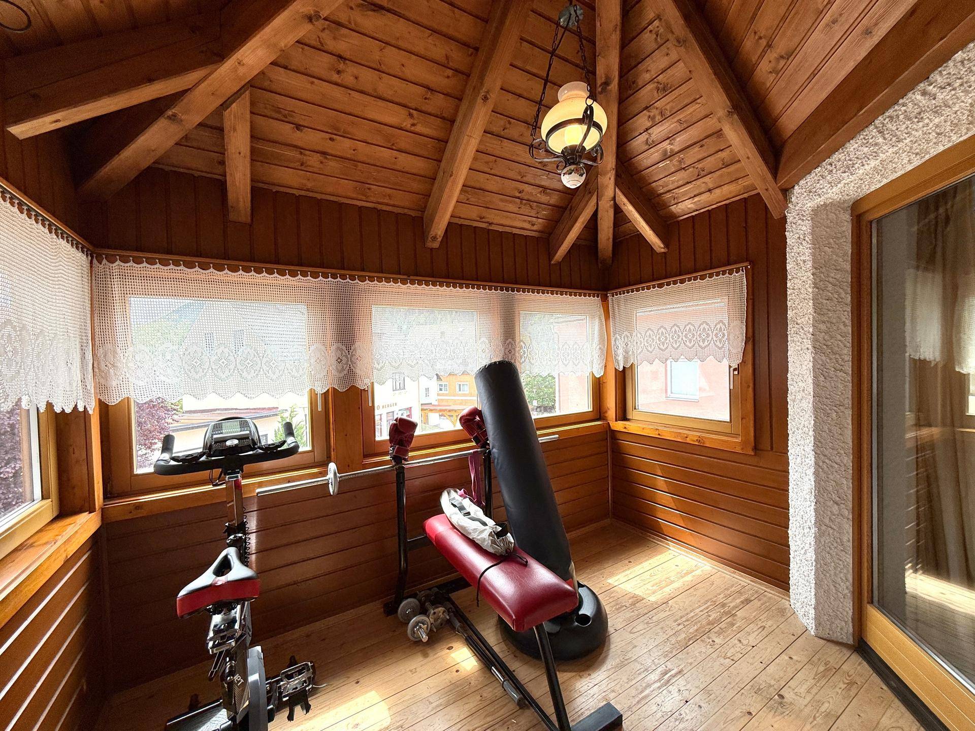 Verglaste Loggia mit Holzverkleidung und Fitnessgeräten, ideal für Sport und Entspannung.