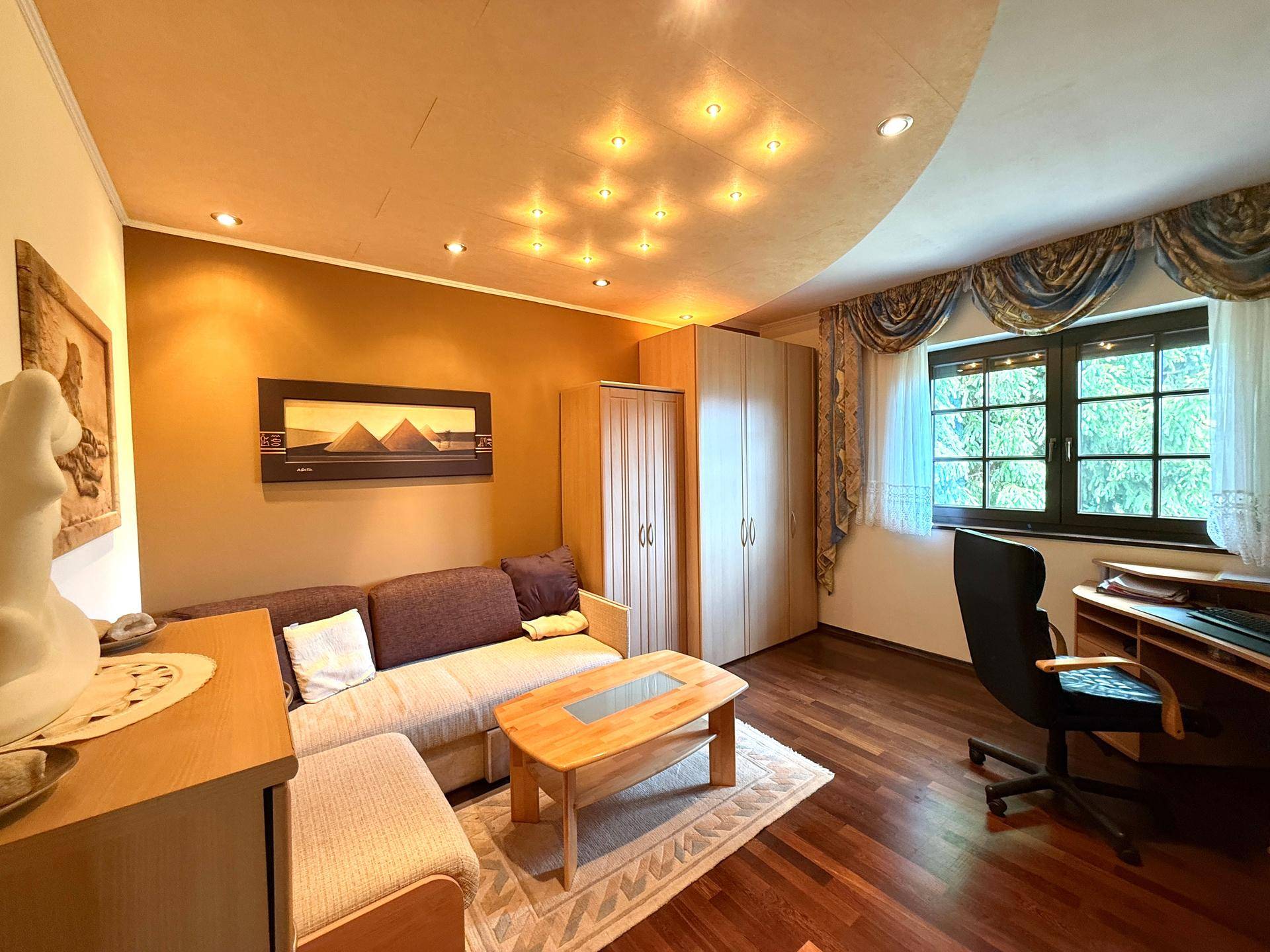 Arbeitszimmer mit Schlafsofa, Schreibtisch und Holzfußboden, ausgestattet mit Deckenstrahlern.