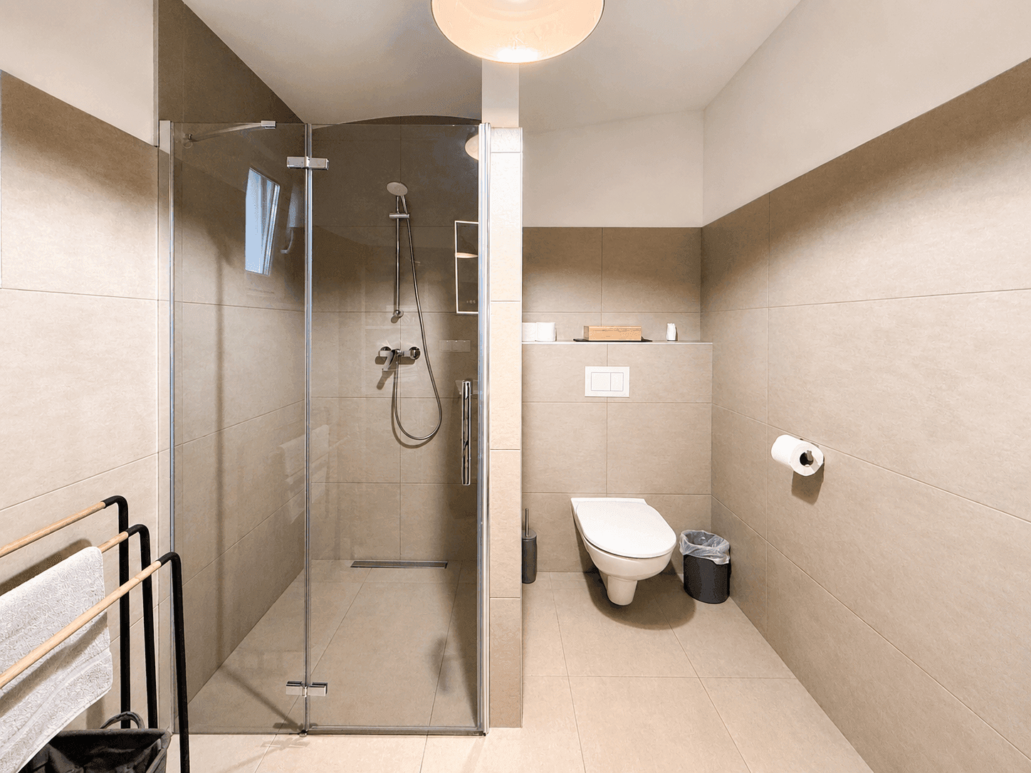 Geräumige begehbare Dusche und Wand-WC in einem modern gefliesten Badezimmer.
