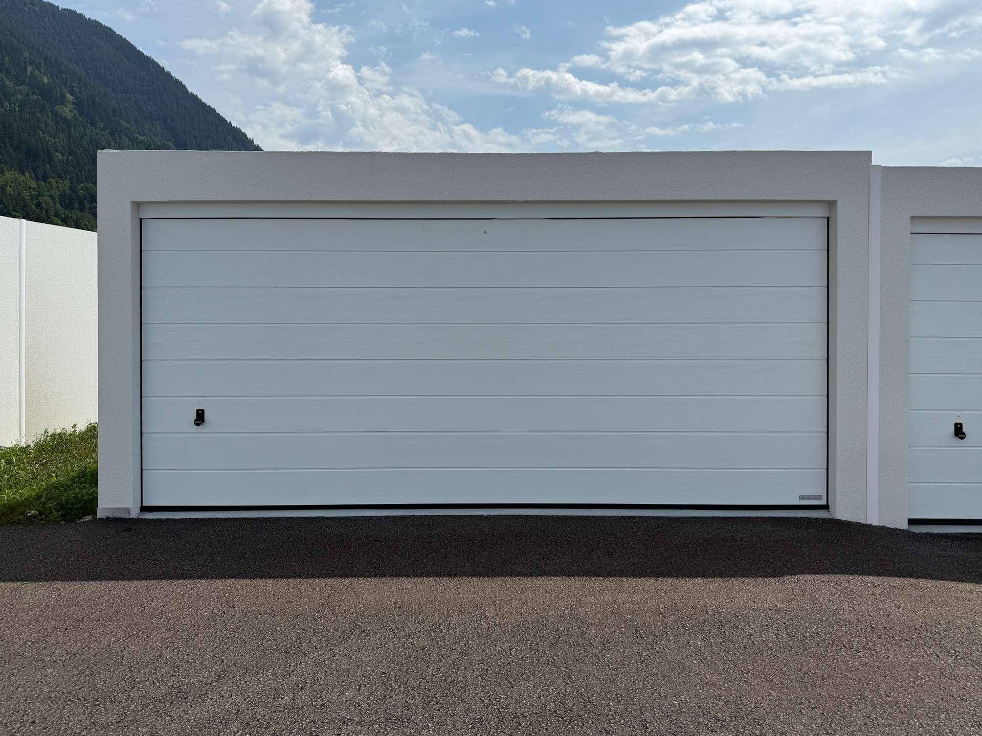 Geschlossene Garagentore einer modernen Garagenanlage vor einer Bergkulisse.
