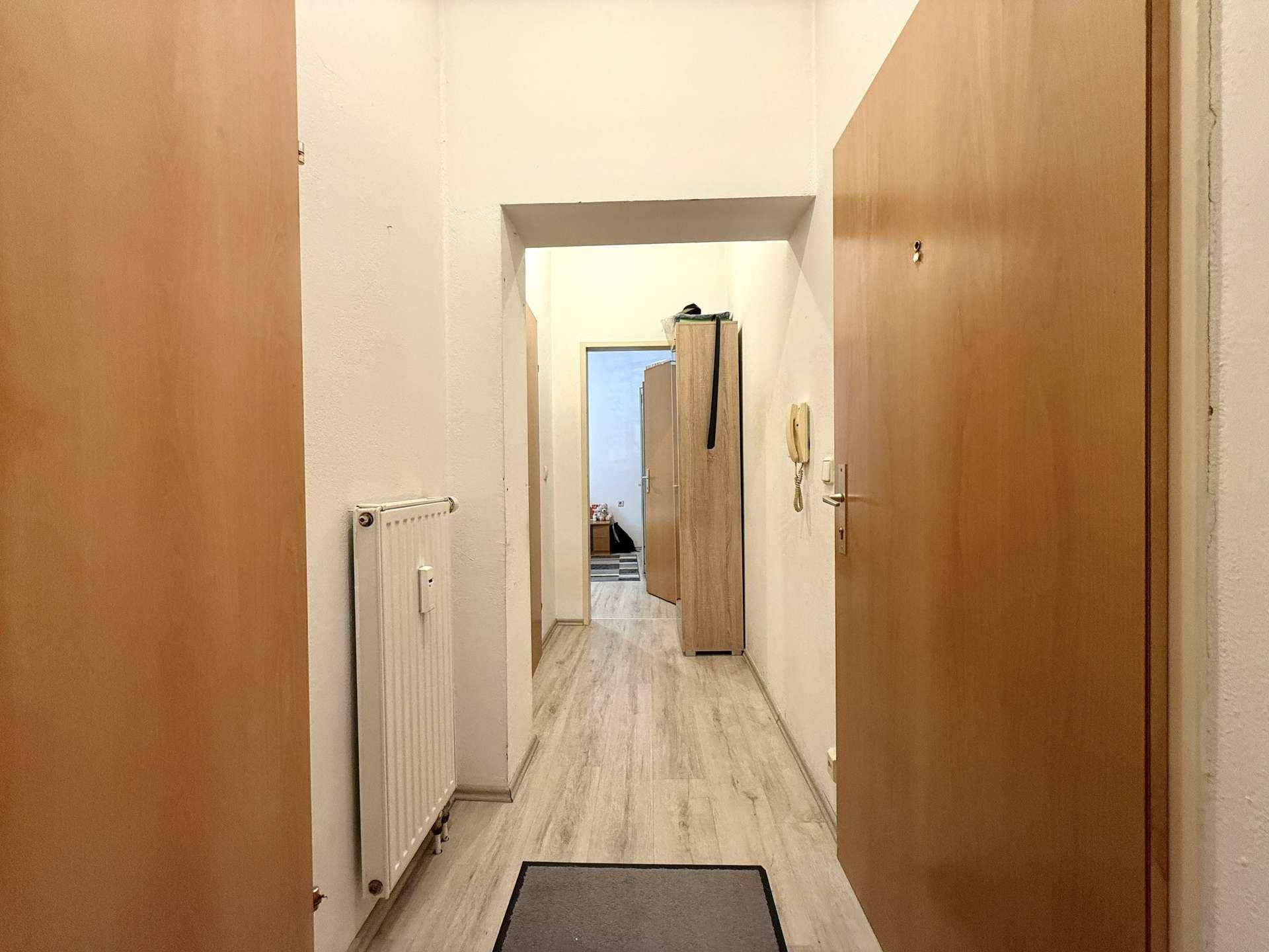 Langer Flur mit Laminatboden, Heizkörper und Holztüren, der zu weiteren Räumen führt.