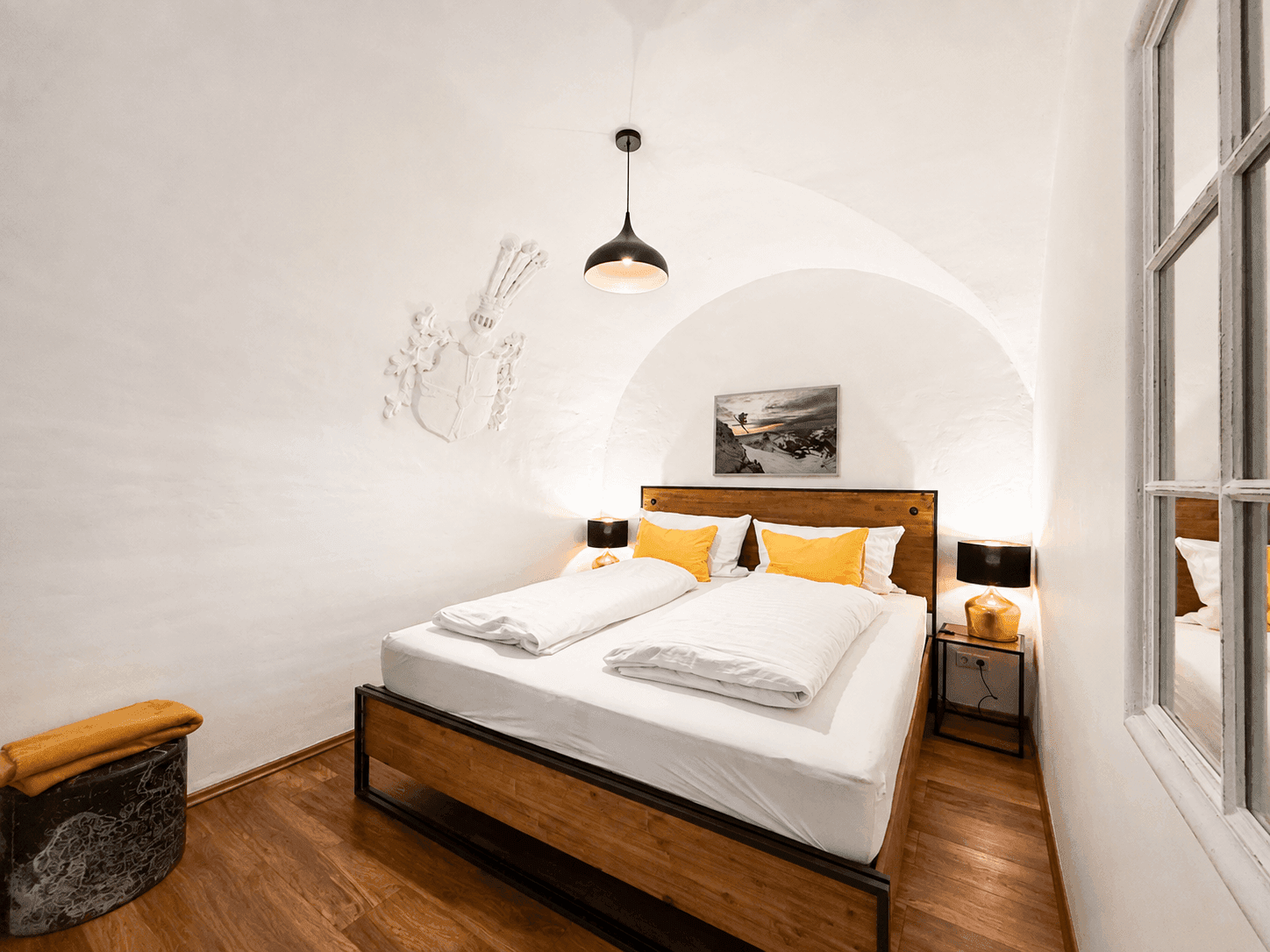 Gemütliches Schlafzimmer mit Holzbett, Holzboden und dekorativem Wappen an der Gewölbedecke.