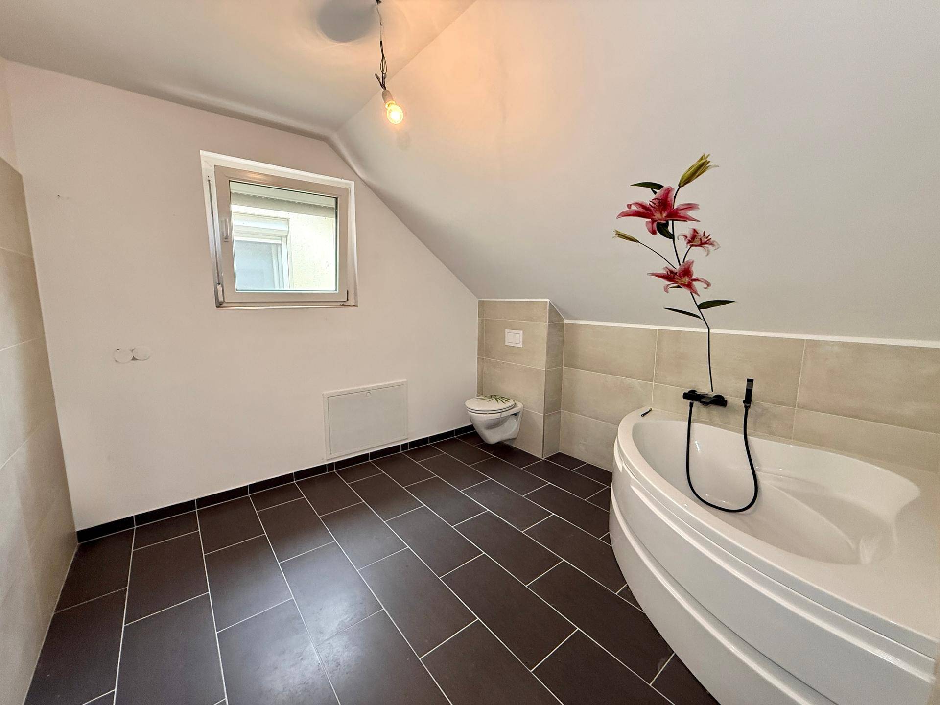 Modernes Badezimmer im Dachgeschoss mit Badewanne, Toilette und dunklen Bodenfliesen.