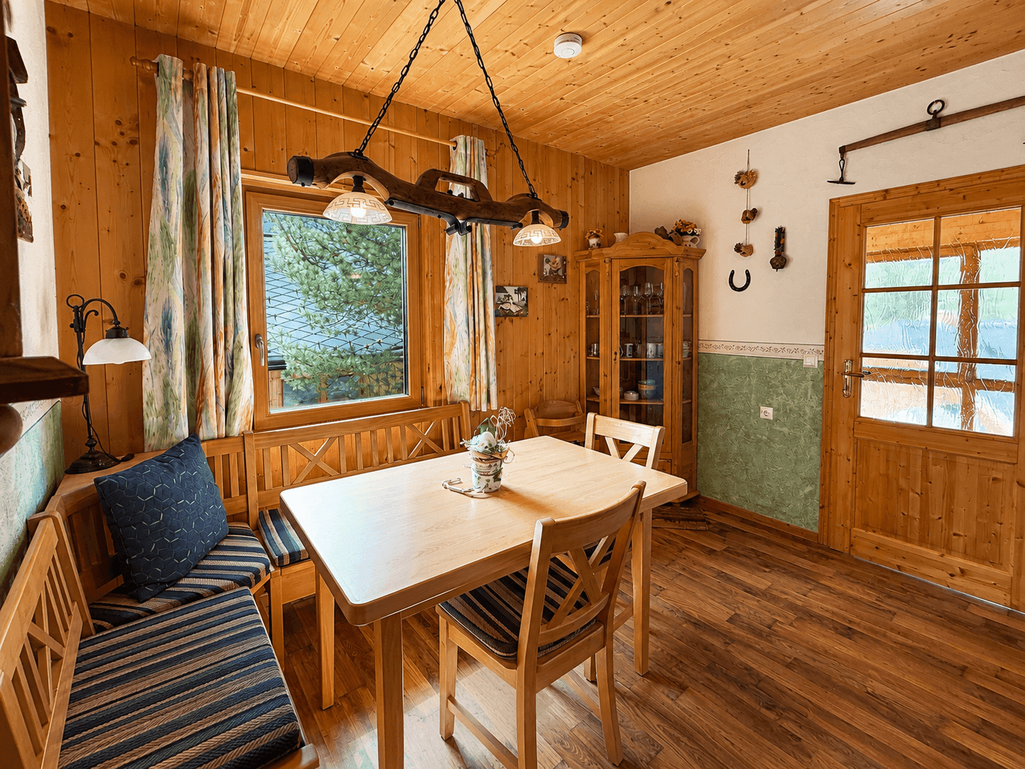 Gemütlicher Essbereich mit Holztisch, Eckbank und Stühlen, umgeben von Holzvertäfelung und Fenstern.