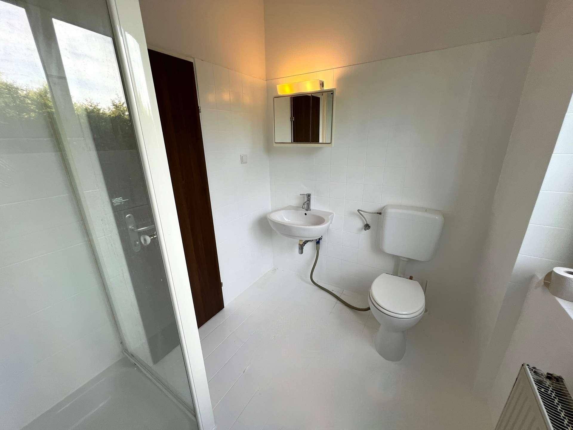 Modernes Badezimmer mit Duschkabine, Waschbecken, WC und Spiegelschrank, hell gefliest.