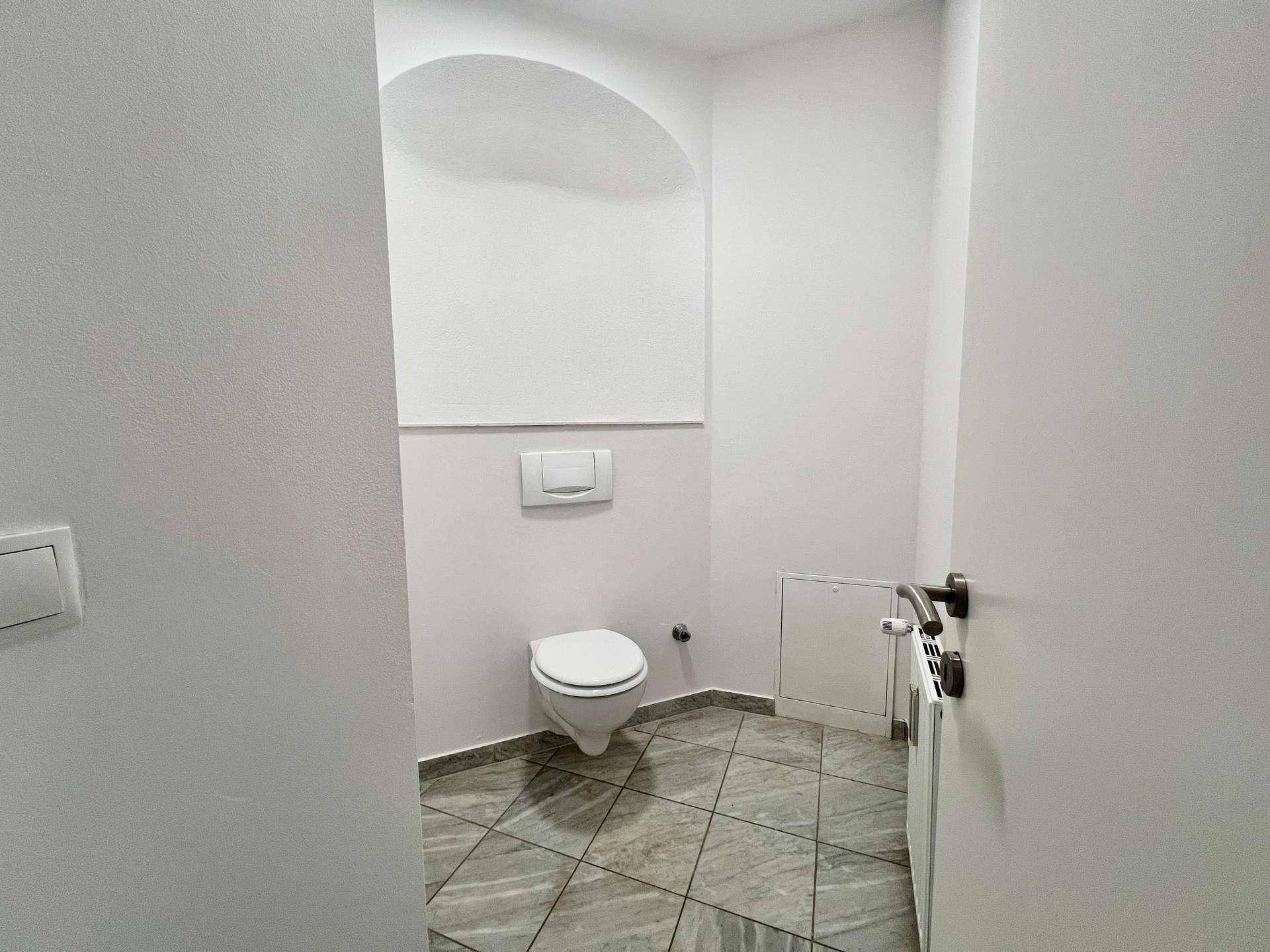 Separate Toilette mit Wand-WC und grauen Bodenfliesen.