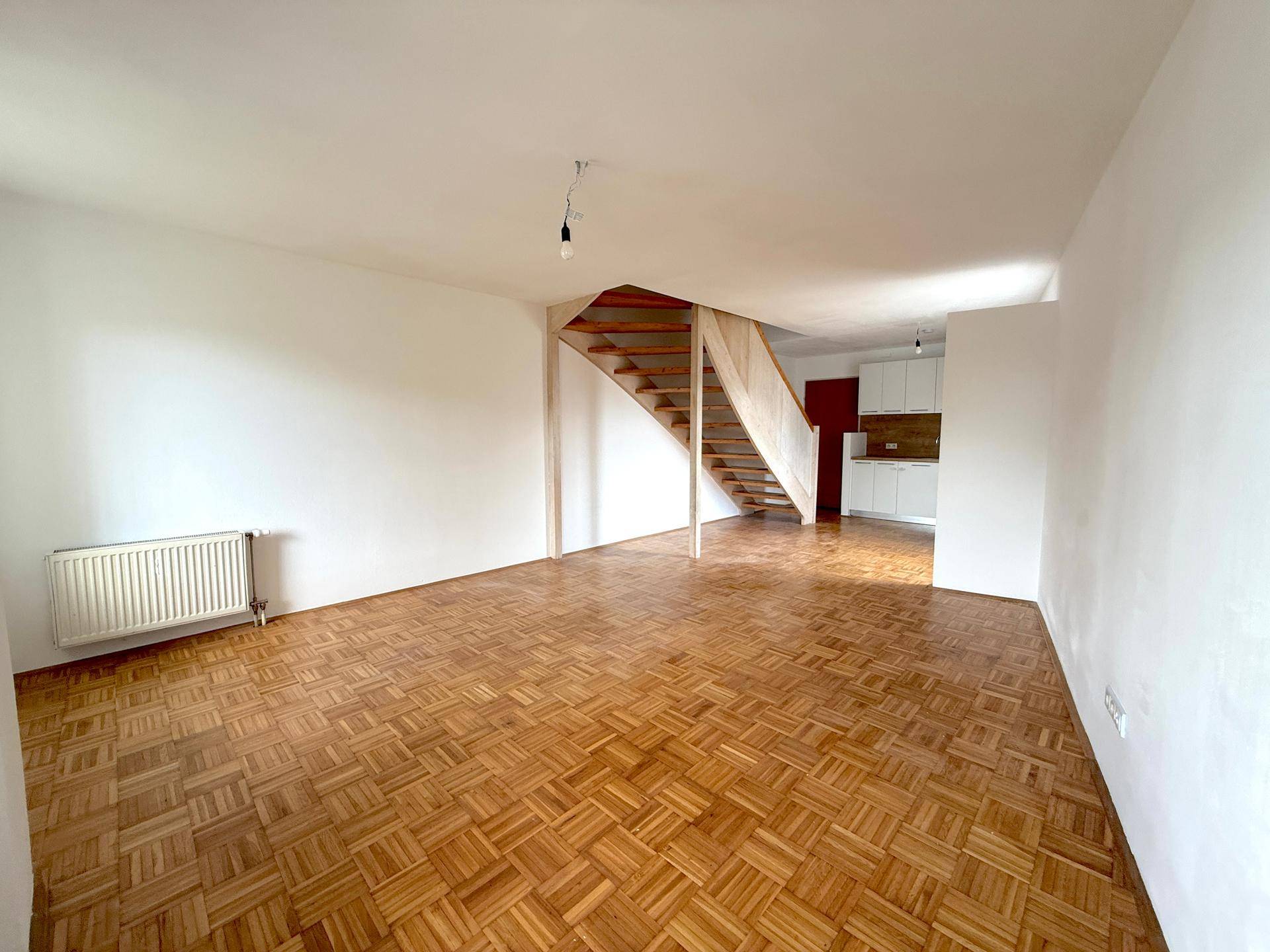 Offener Wohnbereich mit Parkettboden, Holztreppe und Blick auf die moderne Küche.