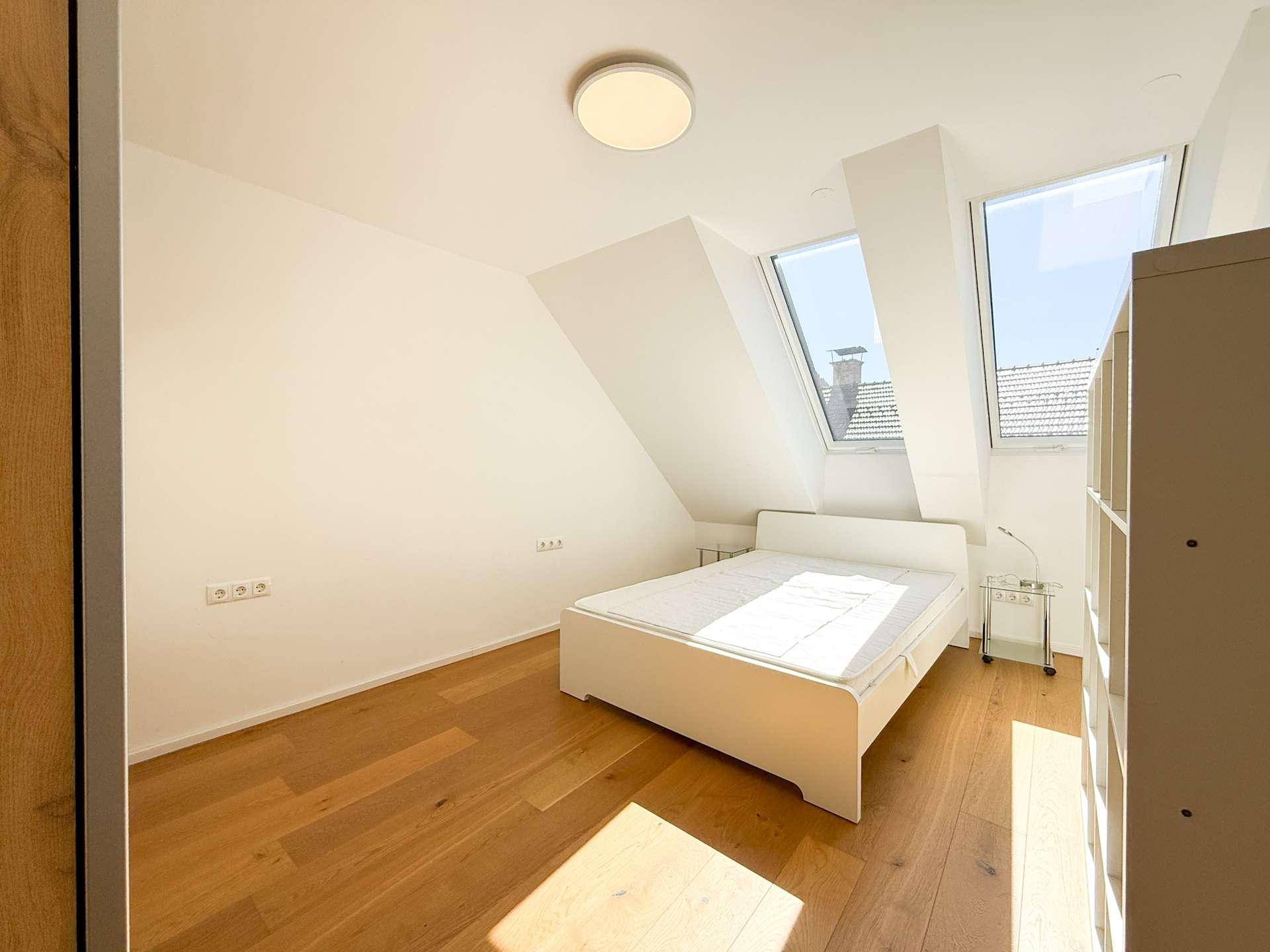 Helles Schlafzimmer mit Holzboden, weißem Bett und zwei Dachfenstern, die viel Tageslicht spenden.