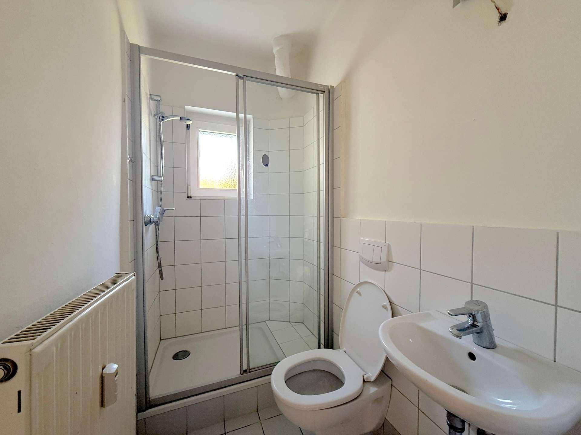 Badezimmer mit Duschkabine, WC, Waschbecken und Fenster, komplett gefliest.