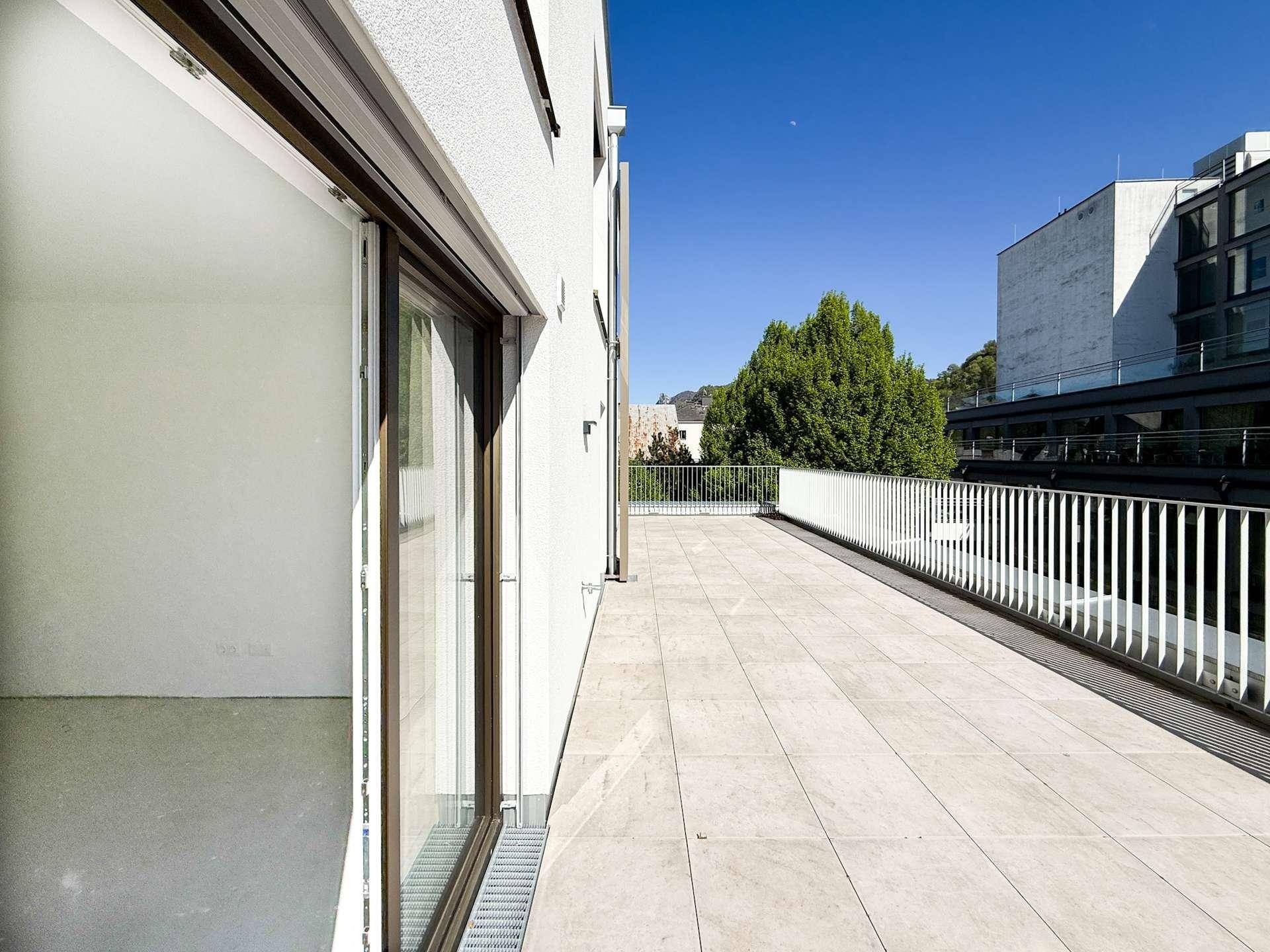 Lange, geflieste Terrasse entlang der modernen Gebäudefassade mit Blick auf die Umgebung.