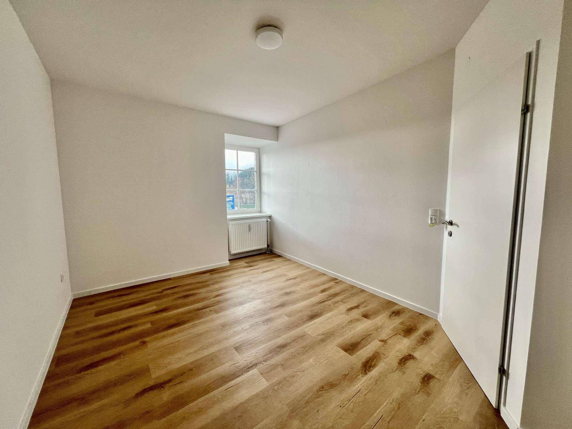 Helles Zimmer mit Laminatboden, weiß gestrichenen Wänden und einem Fenster.