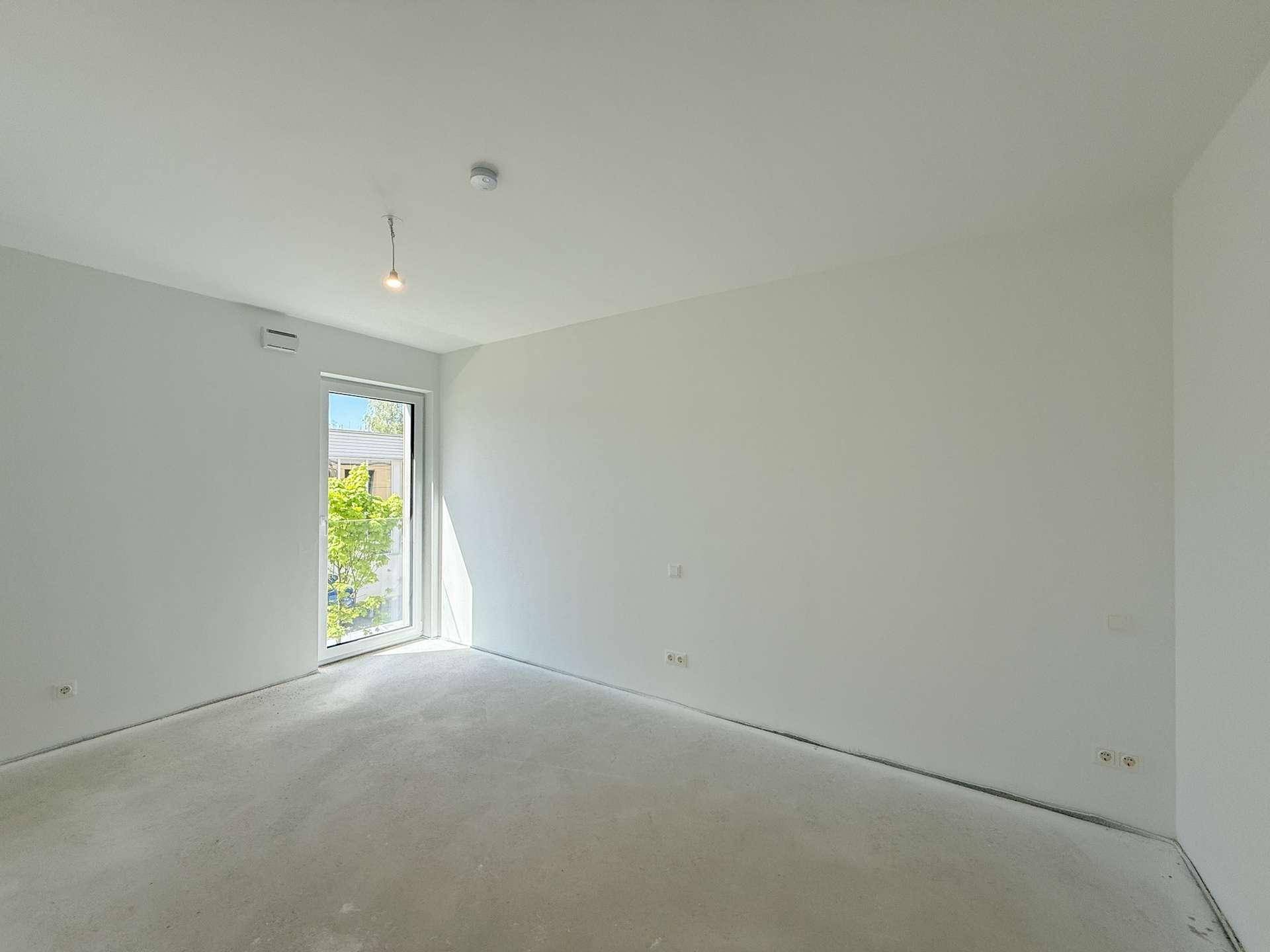 Helles Schlafzimmer im Rohbau mit großem Fenster, das viel natürliches Licht hereinlässt.