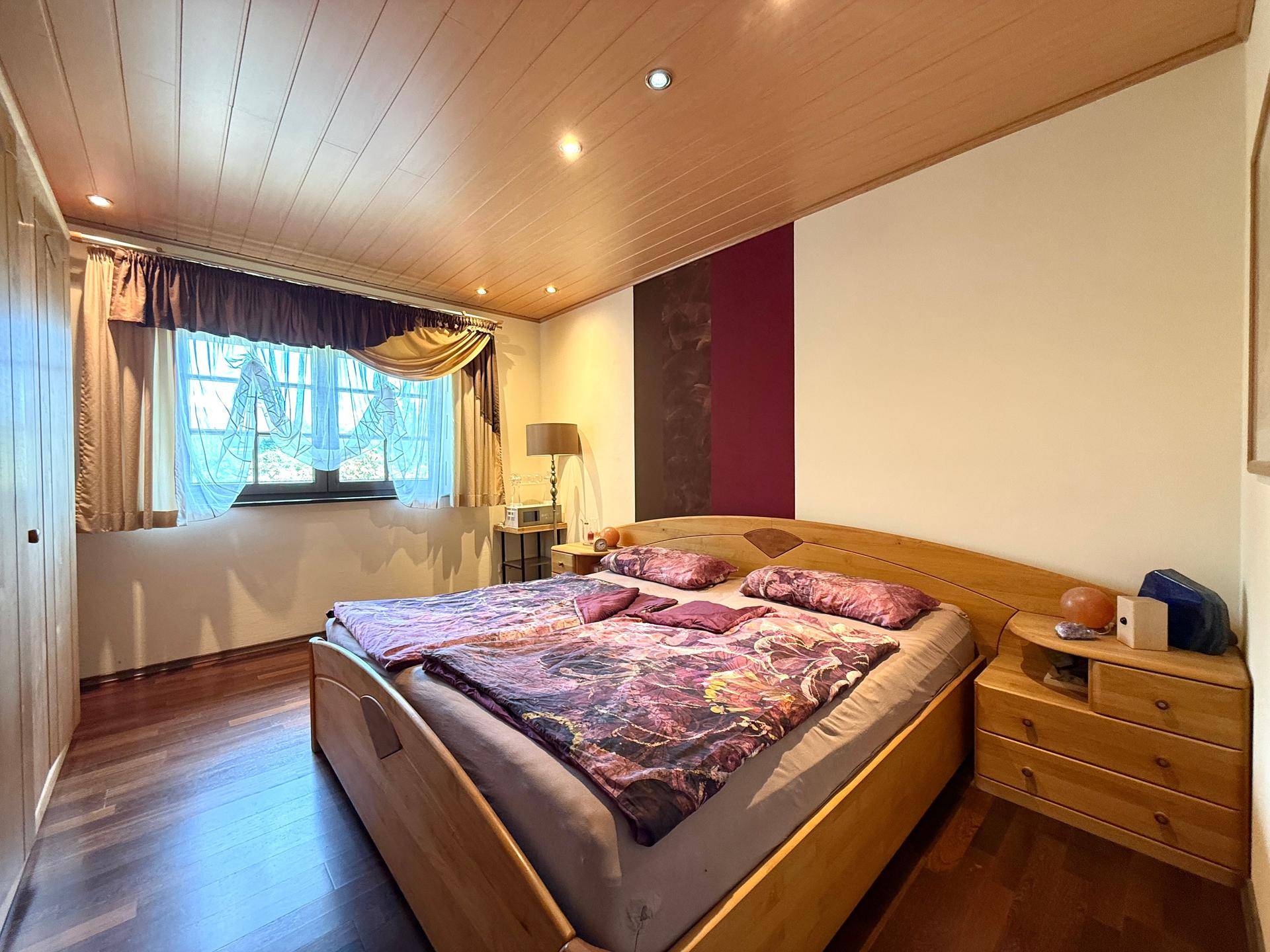 Gemütliches Schlafzimmer mit Holzbett, Nachttischen und Holzdeckenverkleidung.