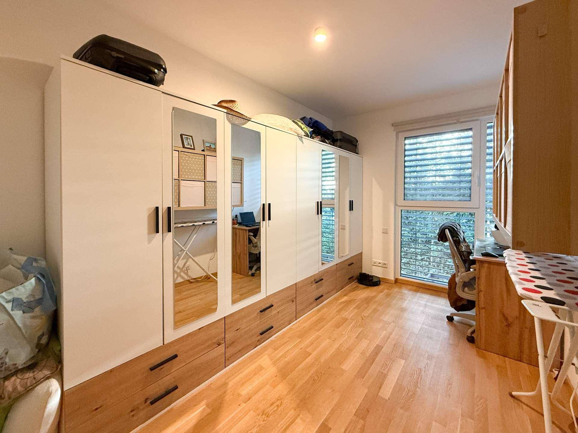 Geräumiges Zimmer mit großem Spiegelschrank, Schreibtisch und Holzboden.