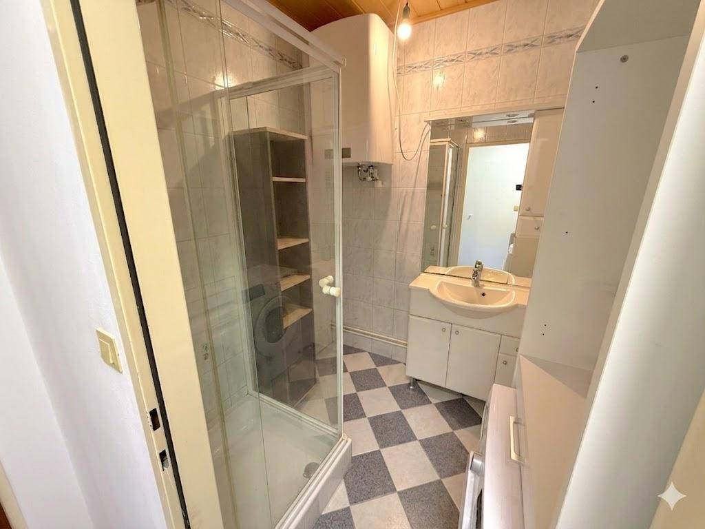 Kleines Badezimmer mit Duschkabine, Waschbecken und schwarz-weiß kariertem Fliesenboden.