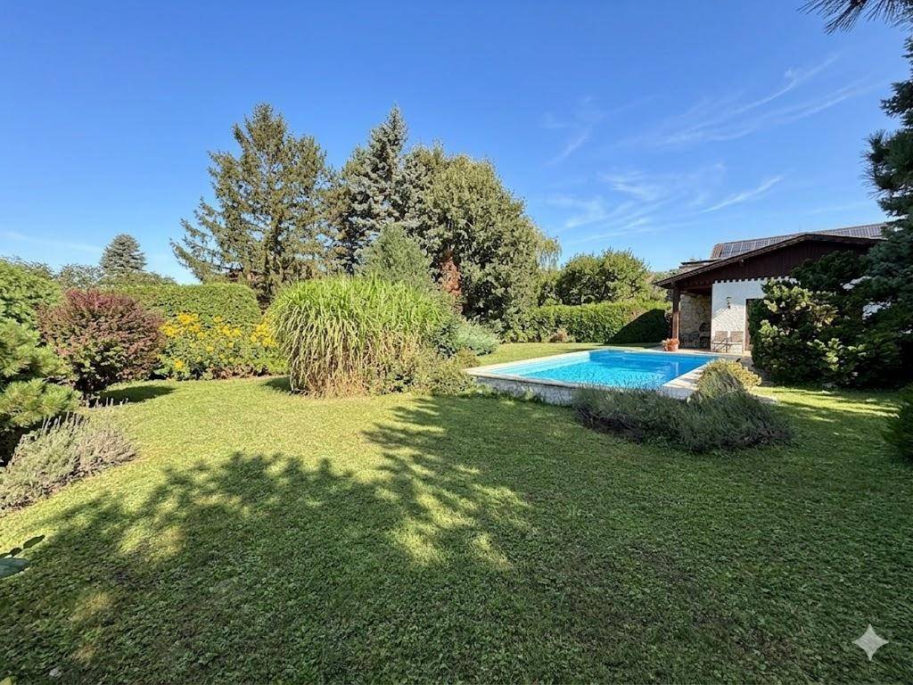 Weitläufiger Garten mit Rasenfläche, umgeben von Bäumen und Sträuchern, mit Blick auf den Pool.