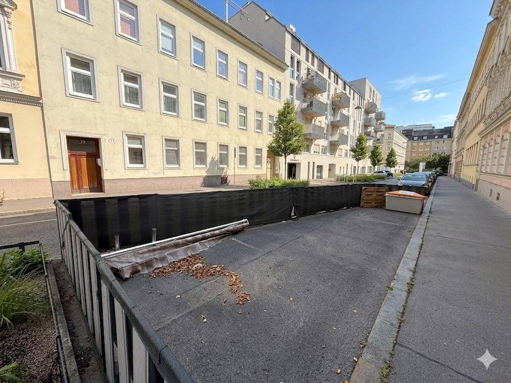 Straßenansicht mit einem Wohngebäude und einem umzäunten Bereich im Vordergrund.