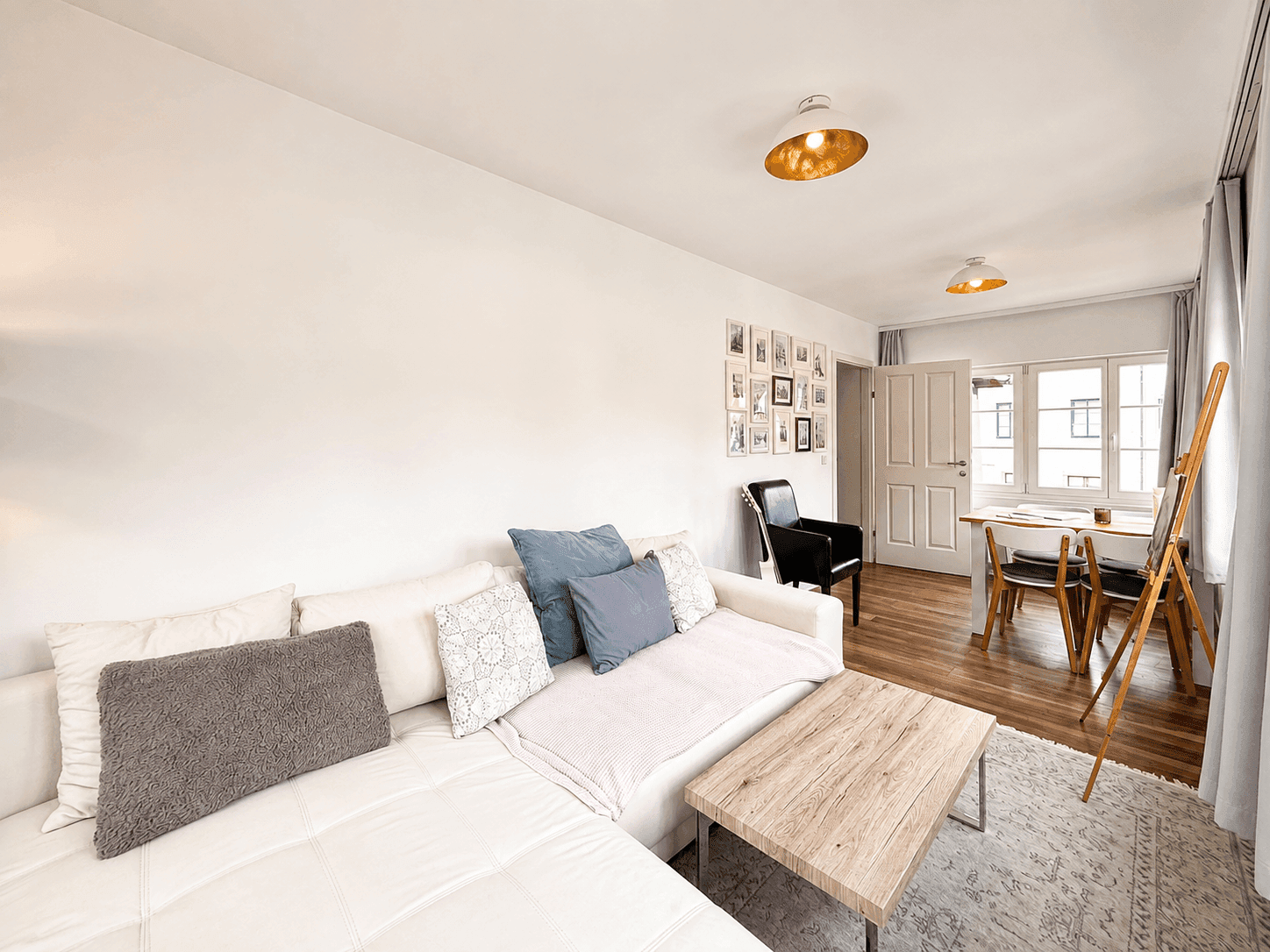 Heller Wohnbereich mit weißem Sofa, Holztisch und gerahmten Bildern an der Wand.
