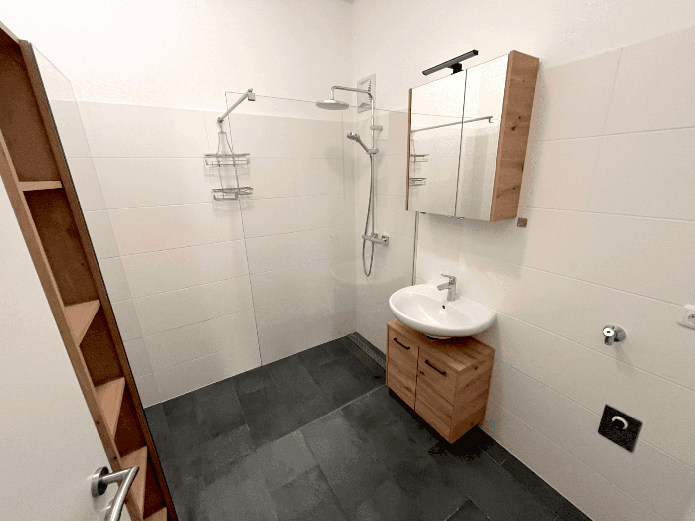 Modernes Badezimmer mit ebenerdiger Dusche, Waschbecken und Holzunterschrank.