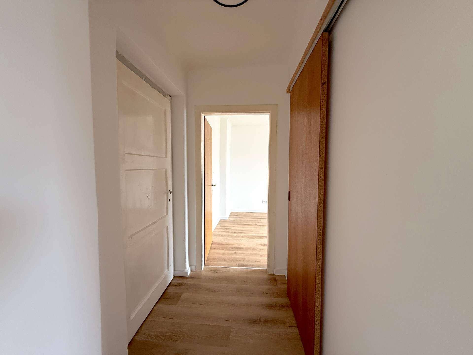 Heller Flur mit Laminatboden und mehreren Türen, darunter eine moderne Schiebetür aus Holz.