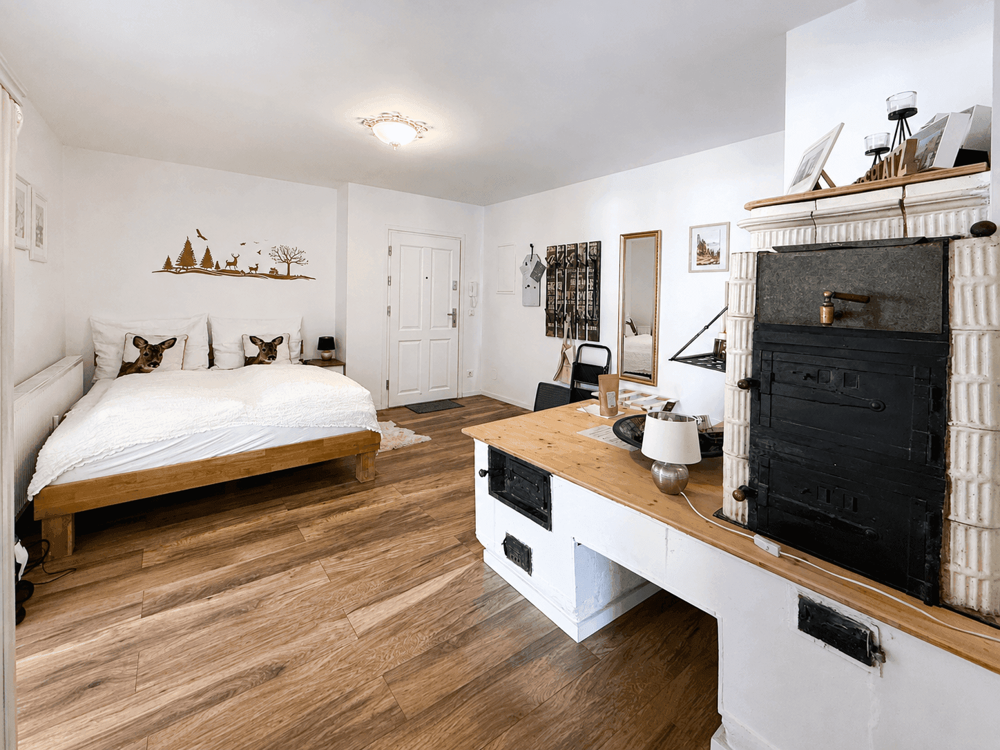 Schlafzimmer mit Holzboden, gemütlichem Bett und einem traditionellen Kachelofen als Blickfang.