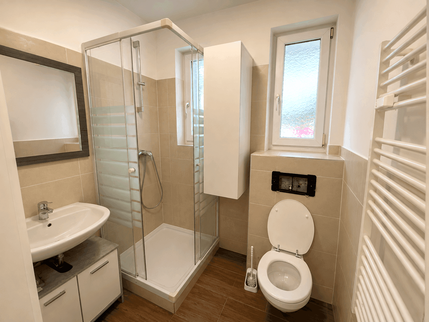 Modernes Badezimmer mit Duschkabine, WC, Waschbecken und beheiztem Handtuchhalter.